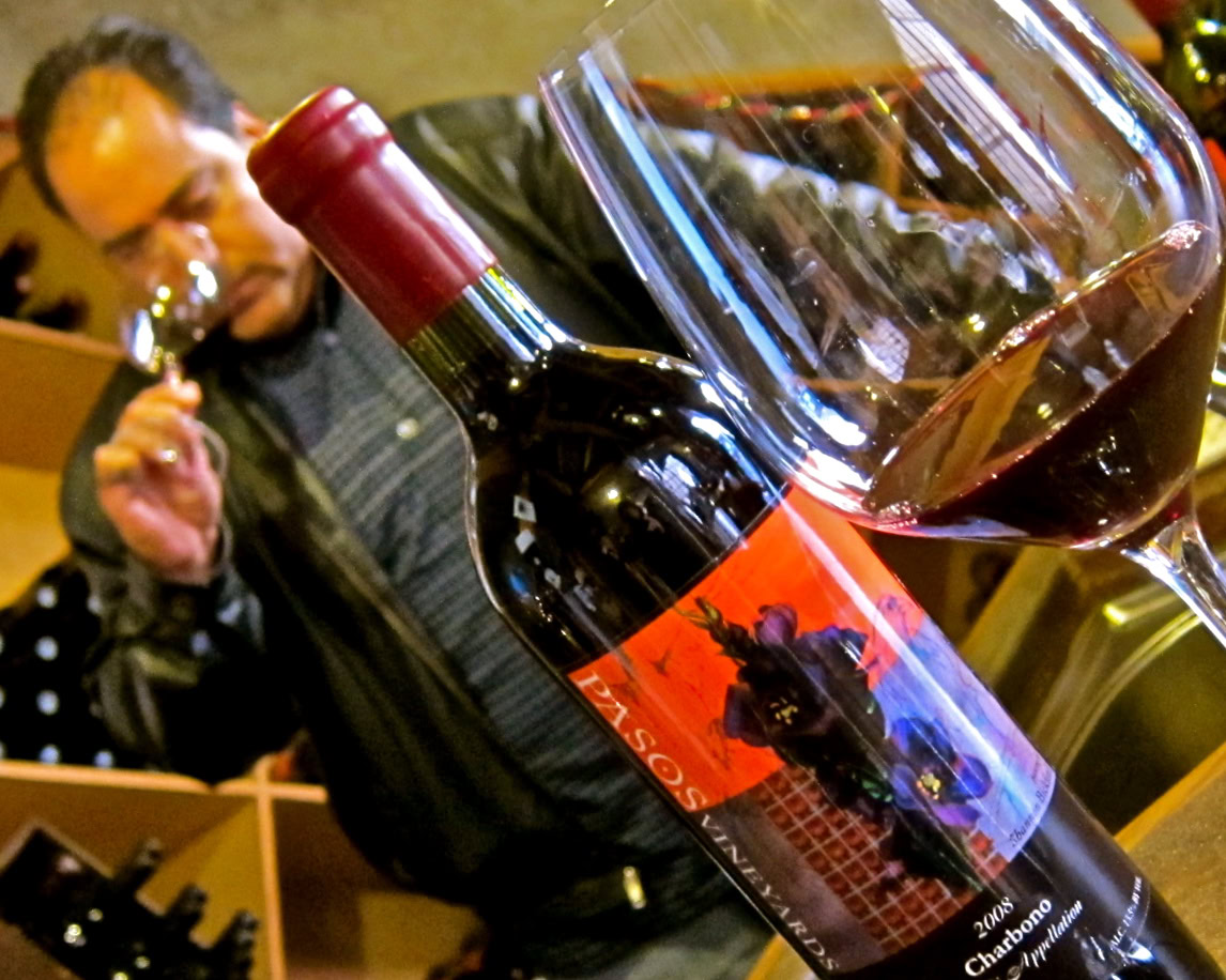 Close-up of a wine bottle and glass with a man tasting wine in the background at a winery event.
