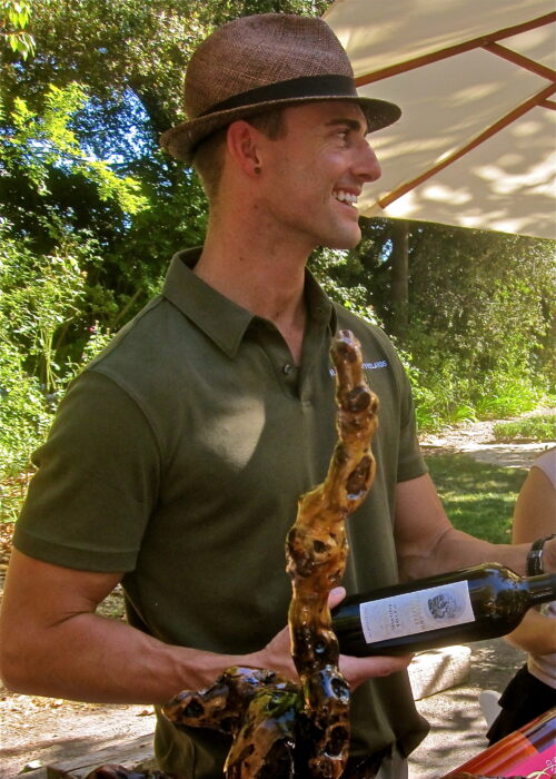 Smiling man holding a wine bottle and a grilled skewer at a Lodi wine event.