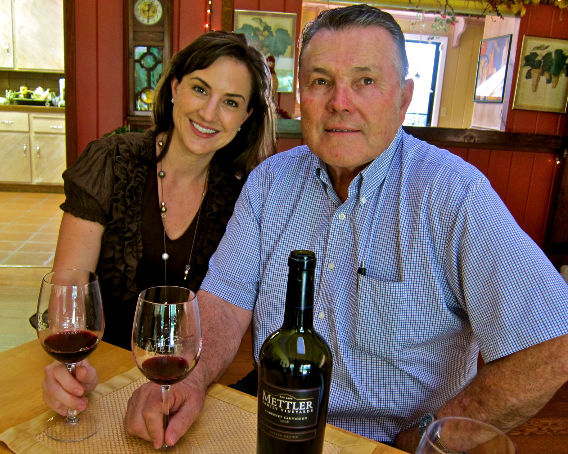 Smiling woman and man at a winery table with wine glasses and a bottle of Mettler wine.