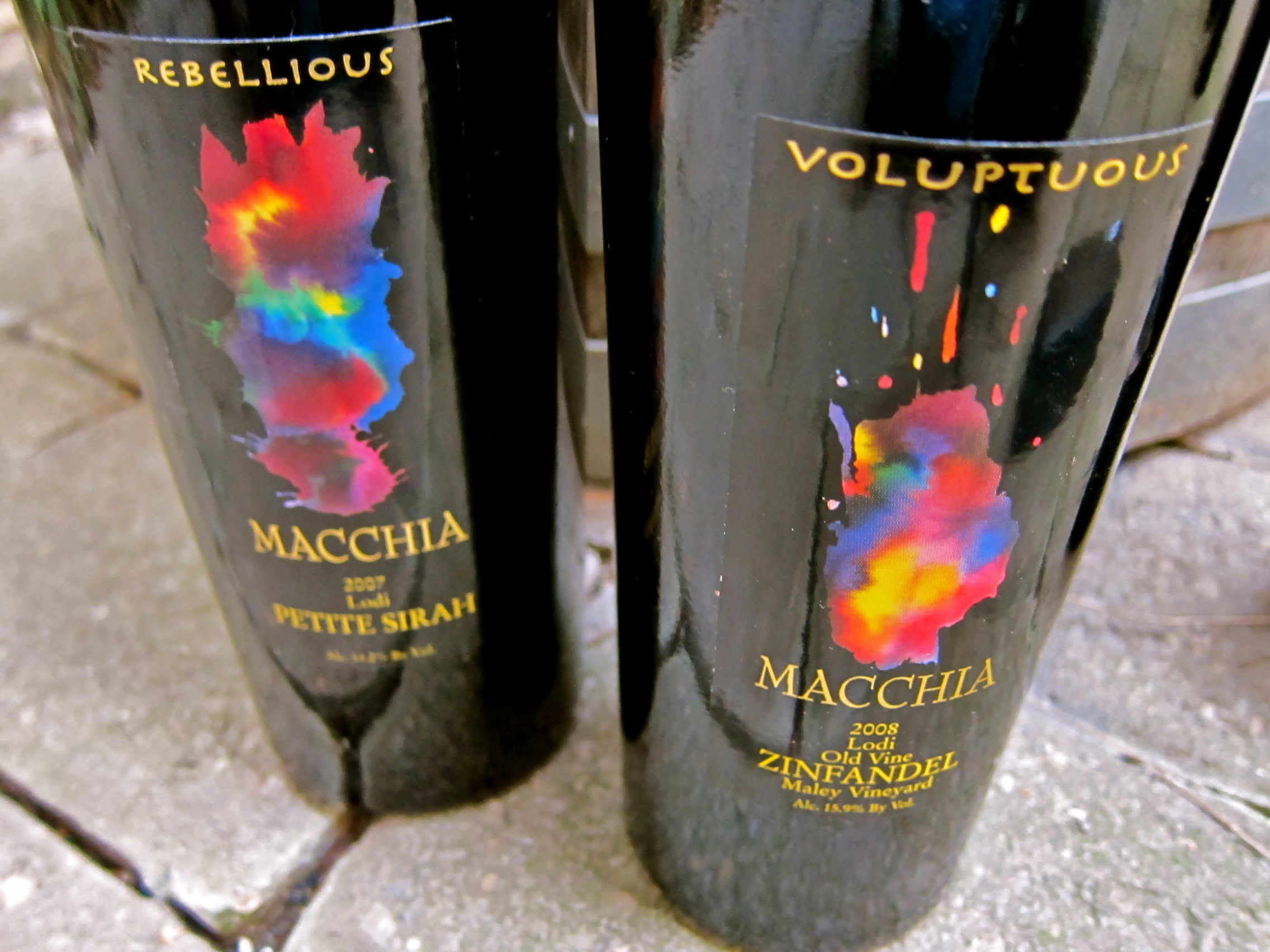Two Lodi Winegrape Commission wine bottles with colorful labels on a brick surface.