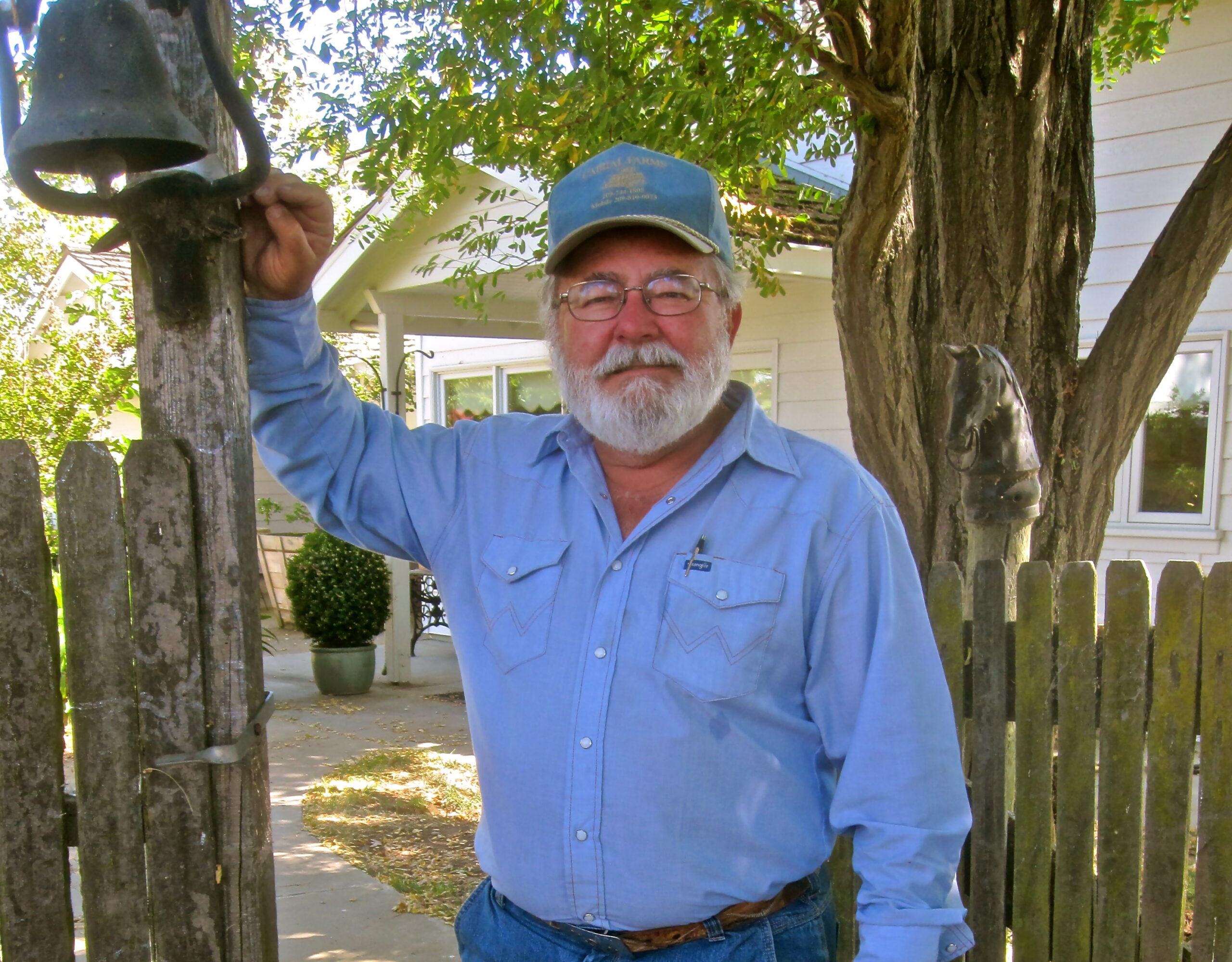 Man with glasses and beard ringing a bell in a garden setting for Lodi Winegrape Commission.
