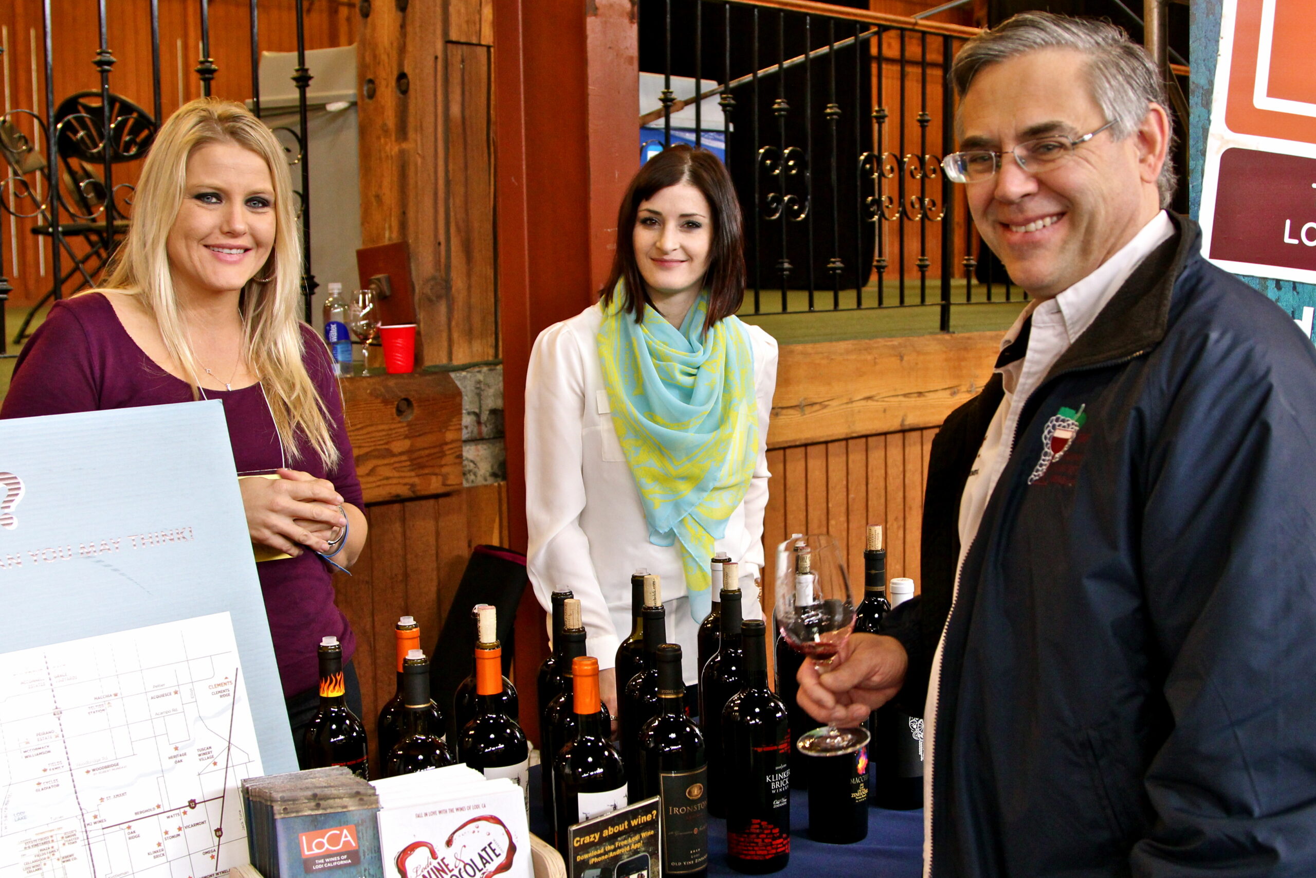 People tasting wine at a Lodi Winegrape Commission event with wine bottles on display.