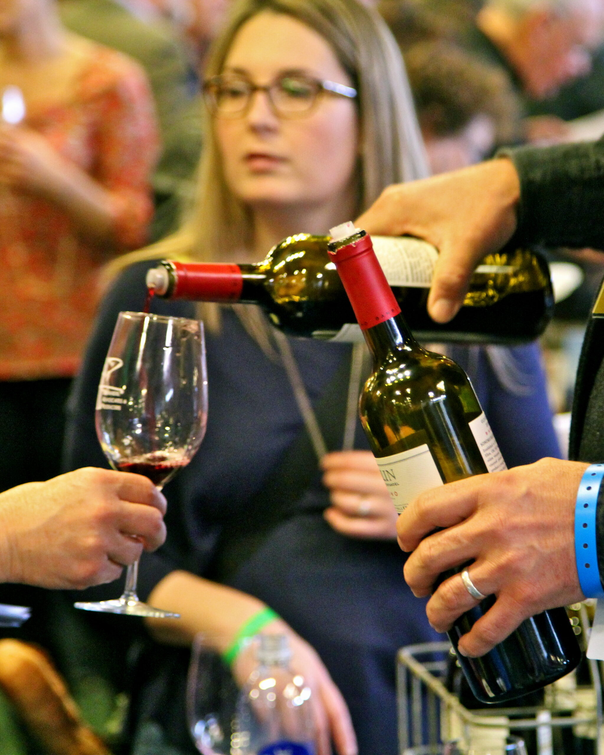 Pouring wine into a glass at a Lodi Winegrape Commission event with attendees in the background.