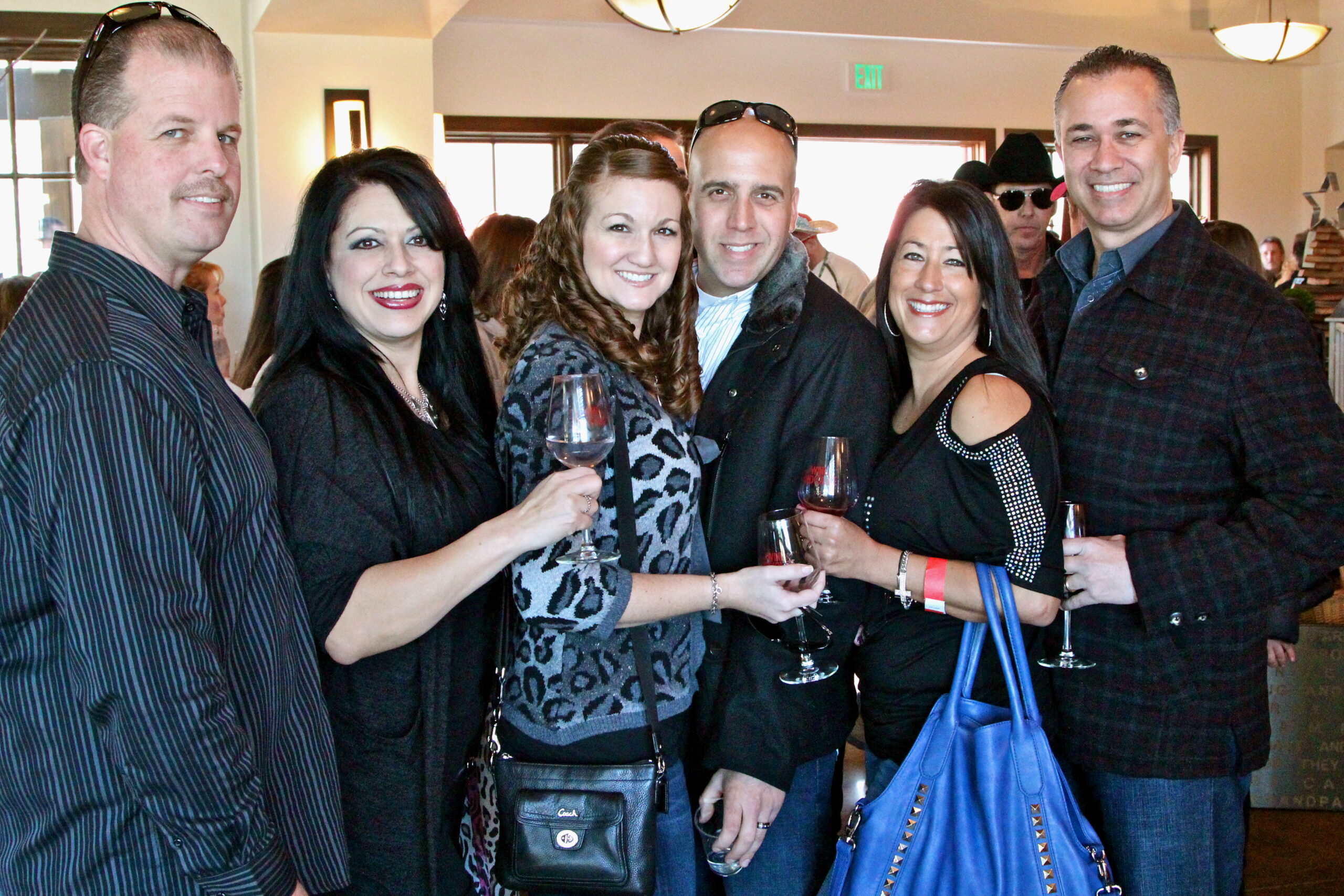 Group of people enjoying wine at Lodi Winegrape Commission event, smiling and holding glasses in a well-lit indoor setting.