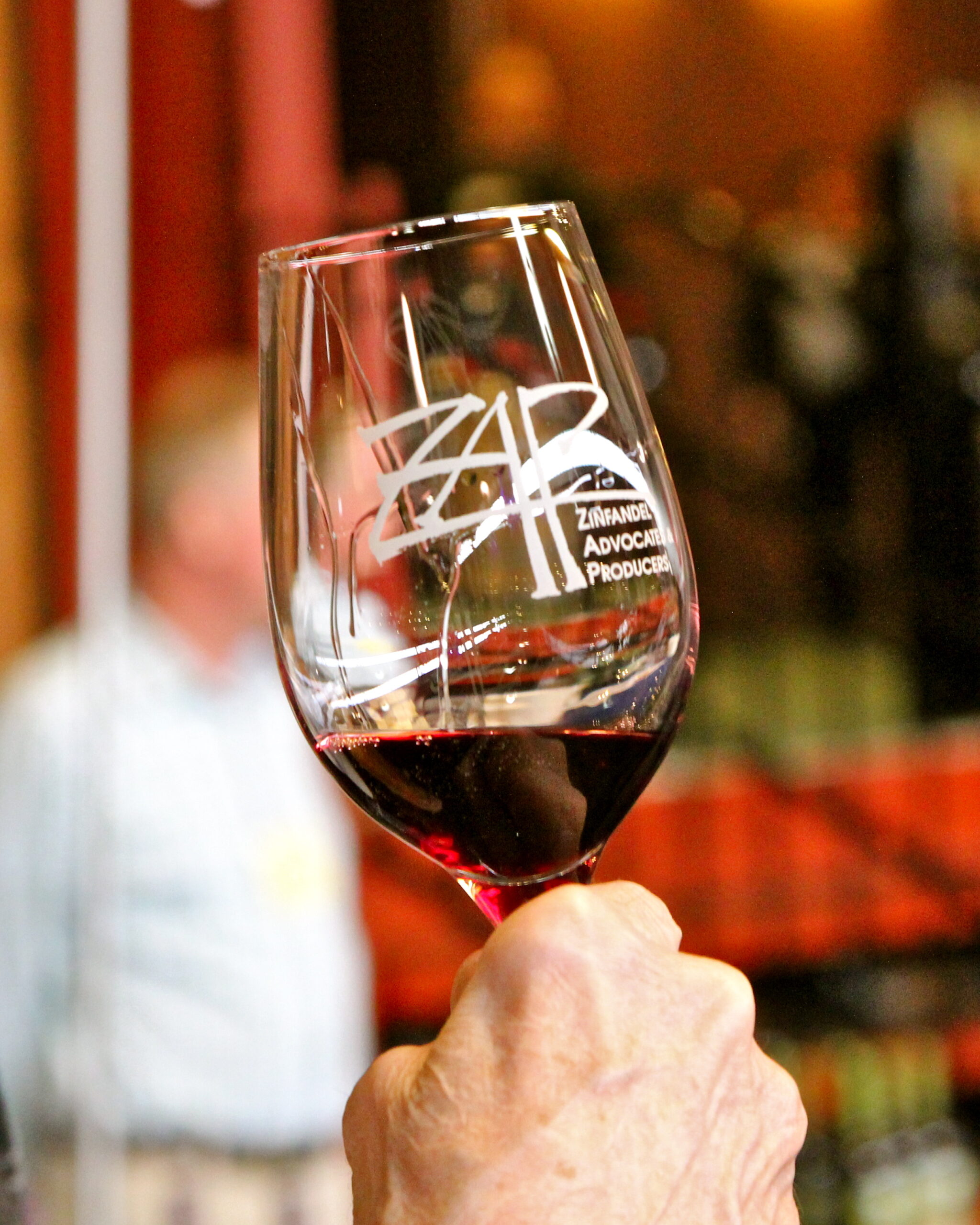 Close-up of a wine glass with Lodi Winegrape Commission logo, filled with red wine, held by a hand.