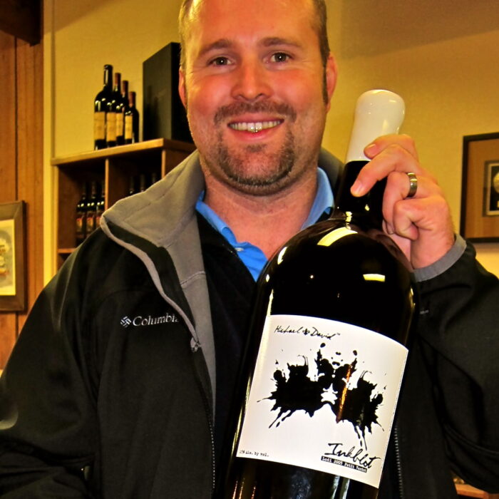 Man holding a bottle of wine with a Lodi Winegrape Commission label in a wine shop.