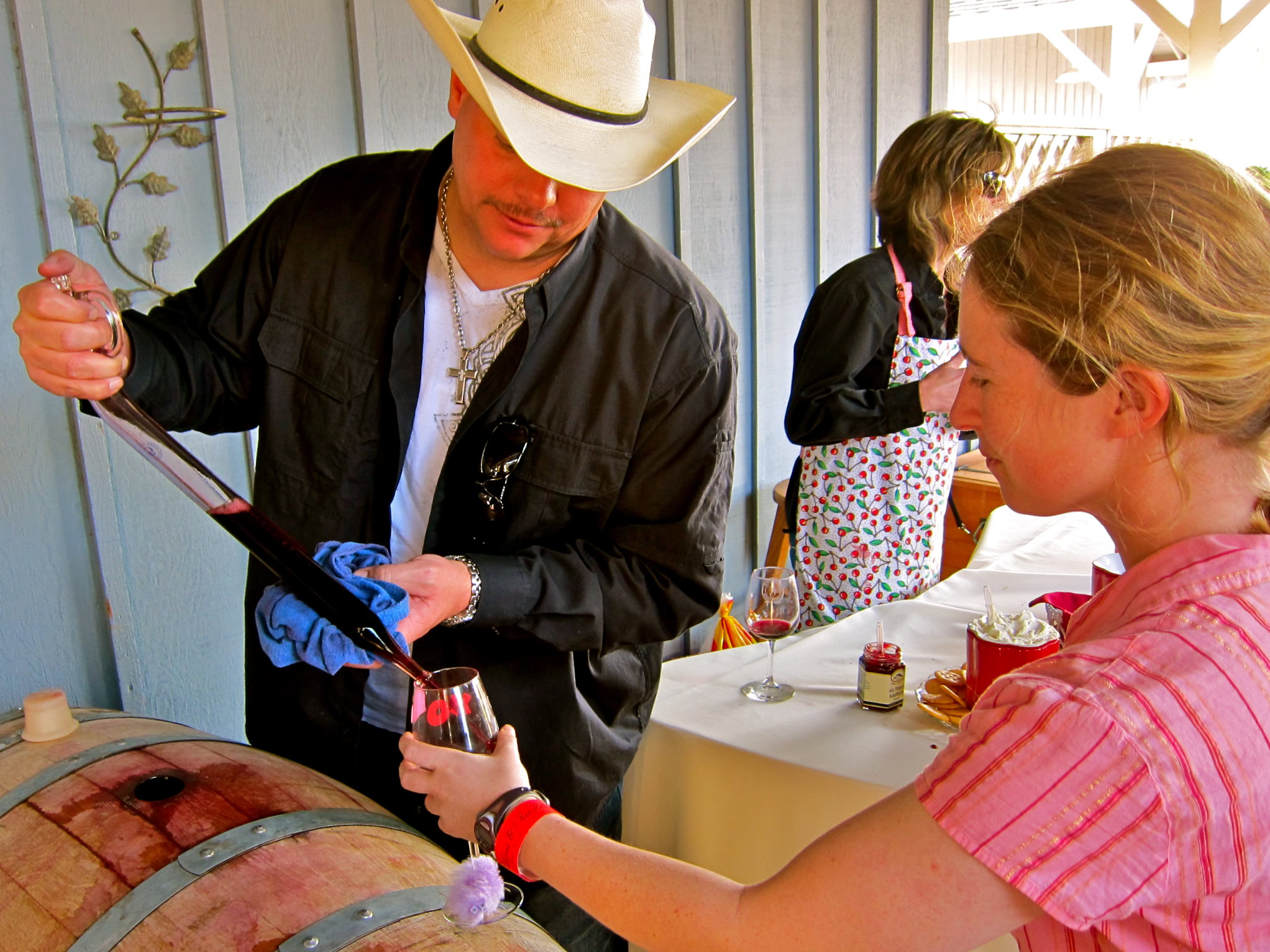Person pouring wine into a glass at a Lodi wine event, with attendees in the background.