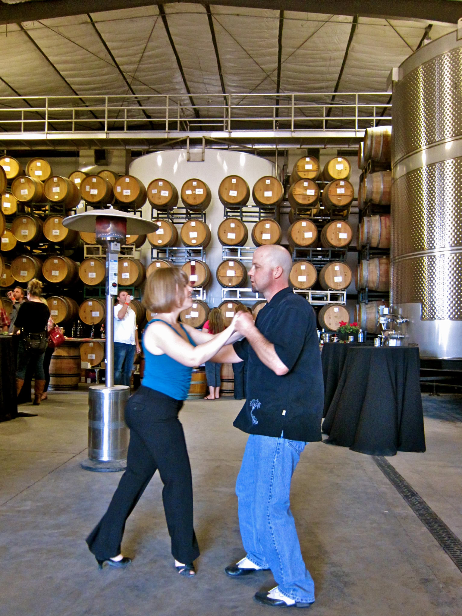 Couple dancing at Lodi Winegrape Commission event with wine barrels in background.