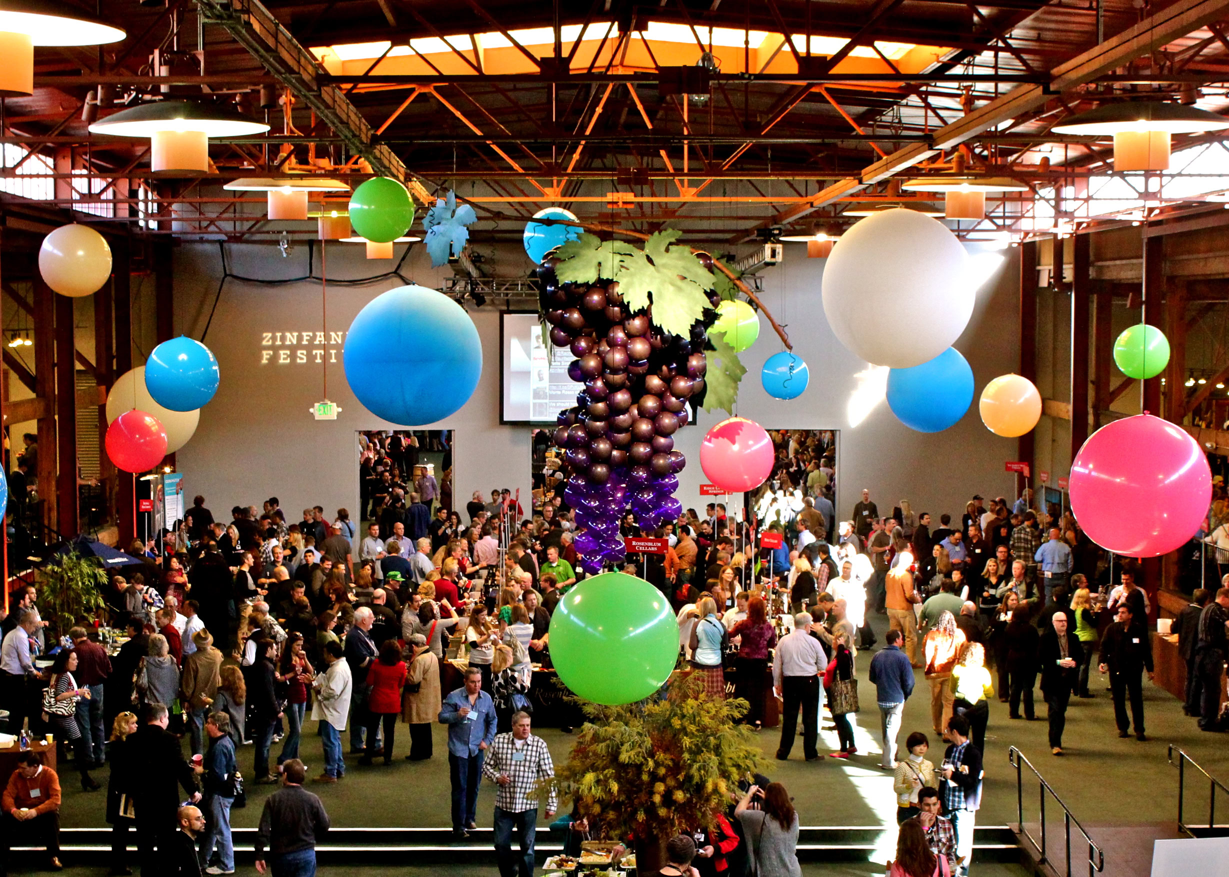 Crowd at Lodi Winegrape Commission event with grape-themed decorations and hanging balloons.