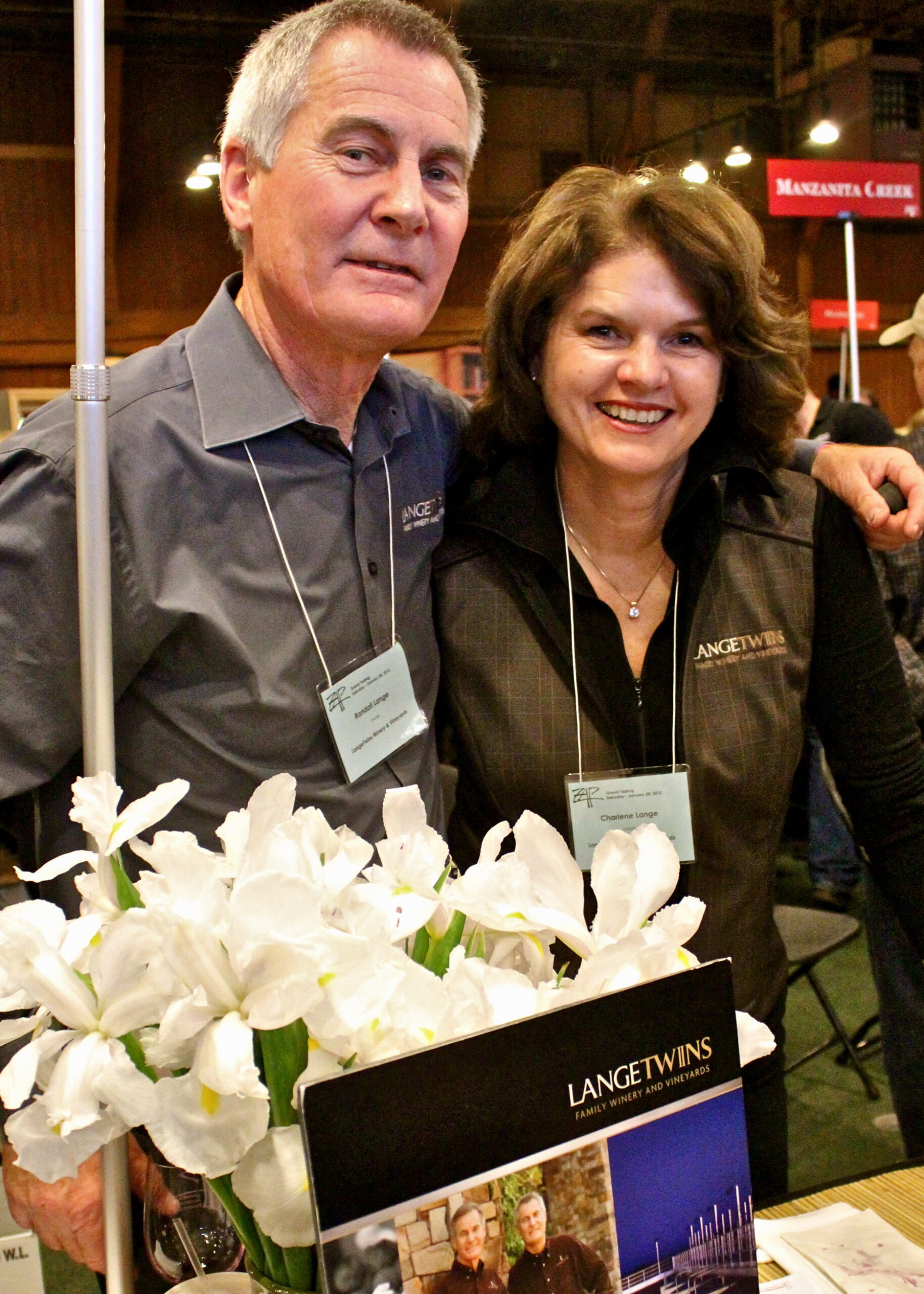 Two smiling individuals at a wine event with Lodi Winegrape Commission branding and flowers in the foreground.