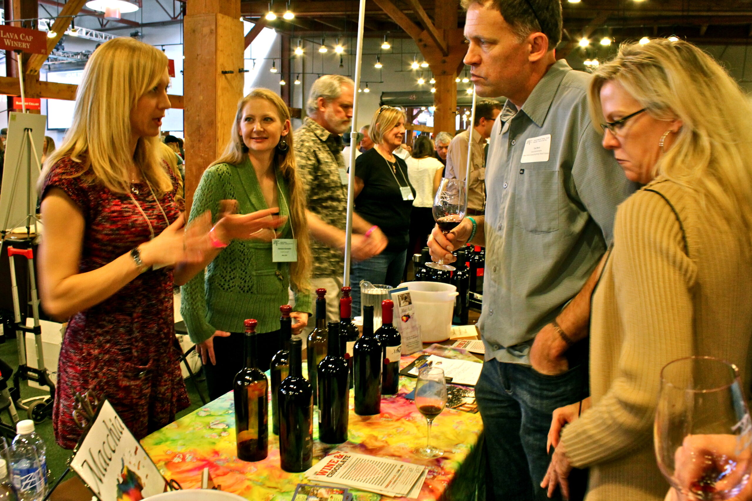 People tasting and discussing wines at a Lodi Winegrape Commission event in a rustic indoor setting.