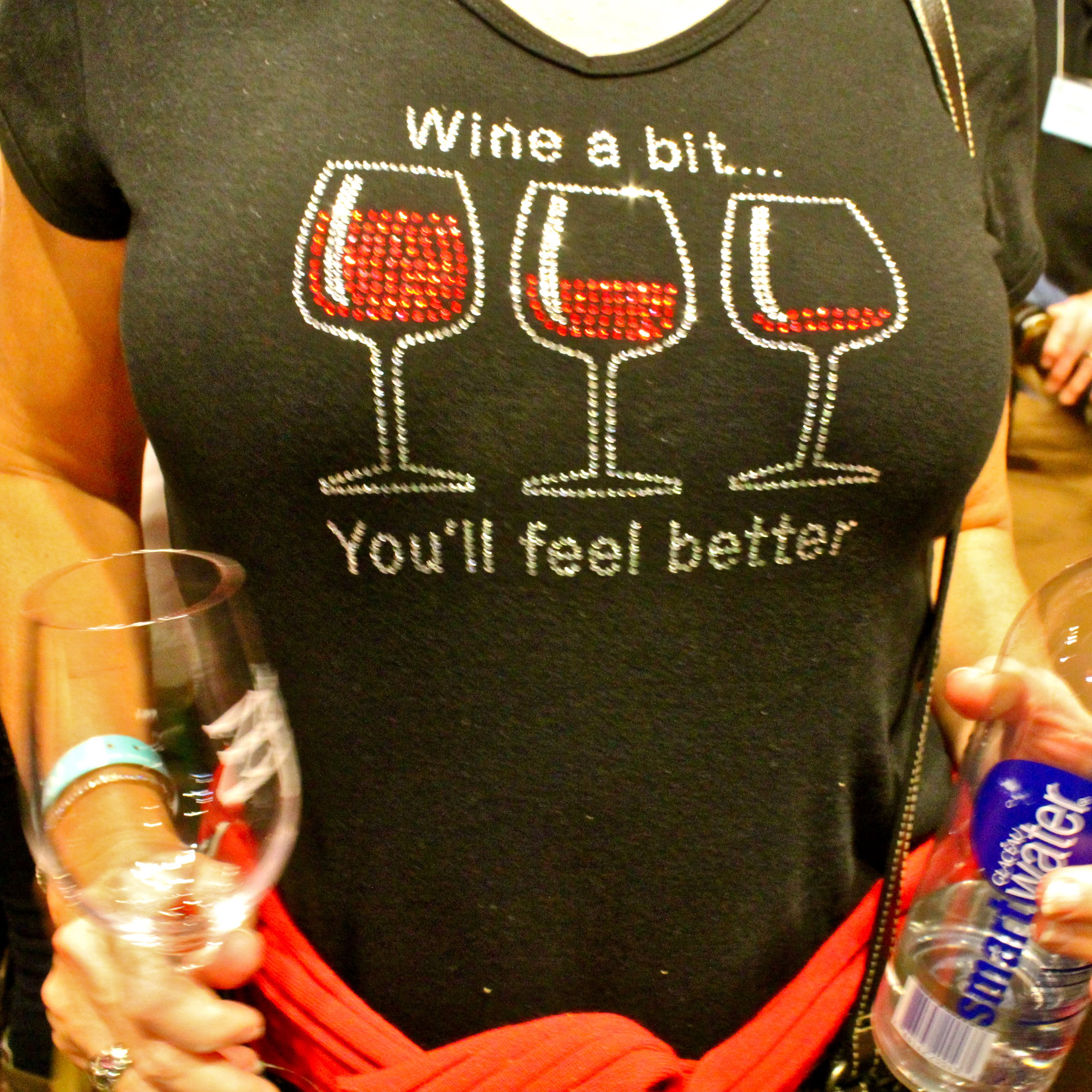 Person holding wine glasses at Lodi Winegrape Commission event, wearing a wine-themed shirt.