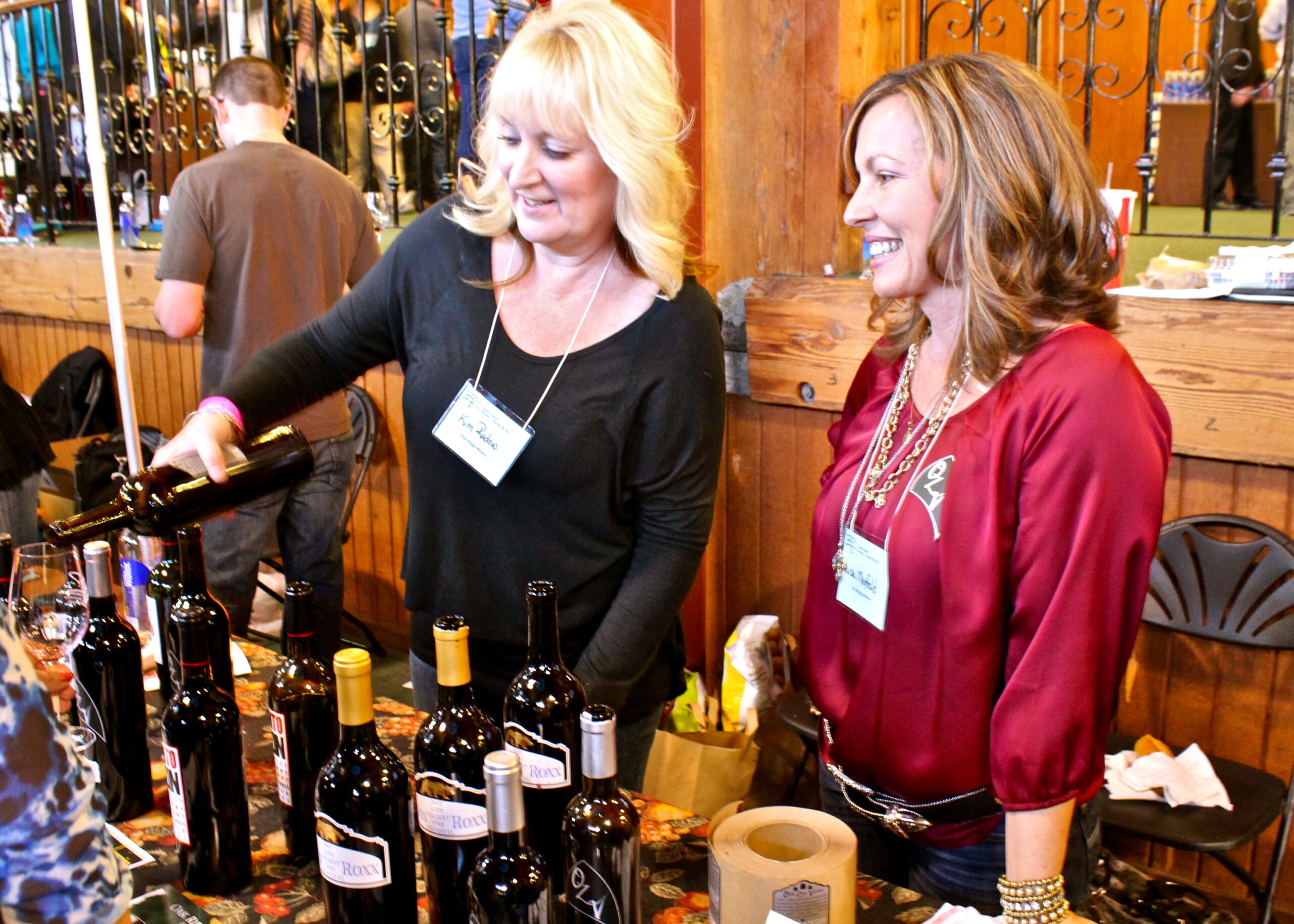 Women enjoying wine tasting at Lodi Winegrape Commission event with bottles on display.