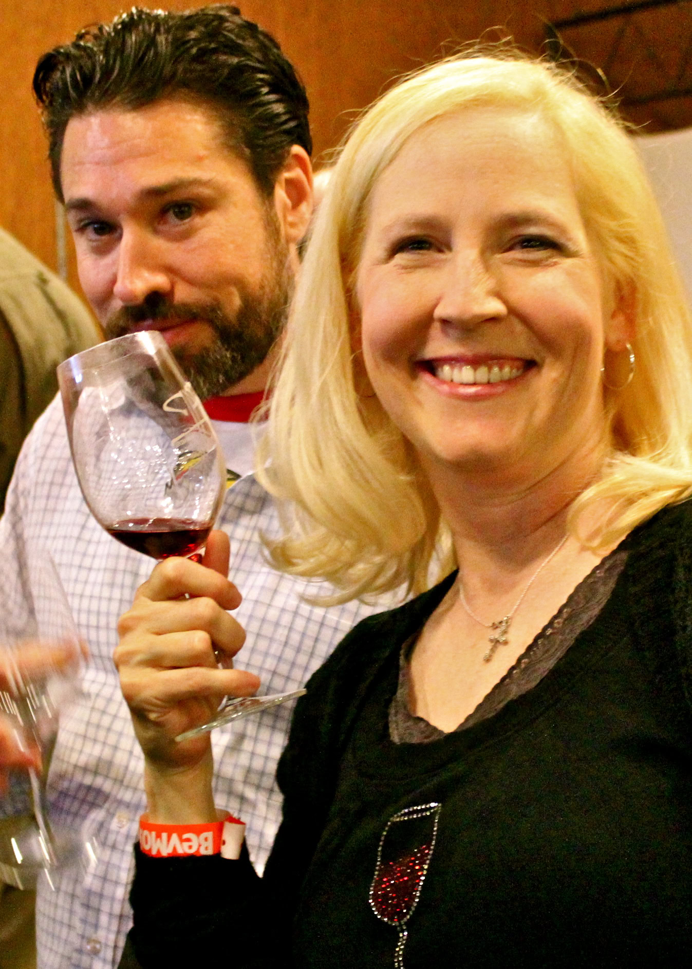 Smiling woman holding a glass of red wine at a wine tasting event.