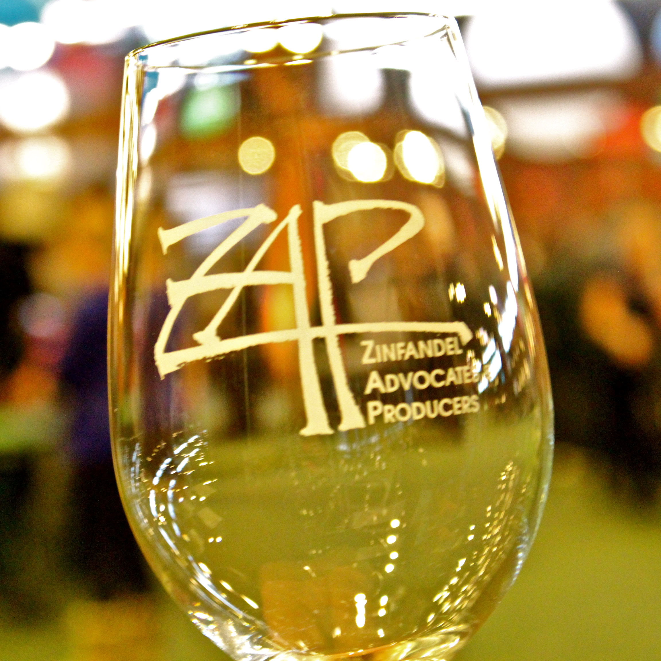 Close-up of a wine glass with Lodi Winegrape Commission logo, filled with white wine, in a winery setting.