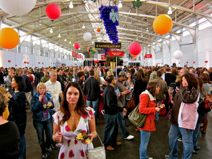 Crowd at a wine event organized by the Lodi Winegrape Commission in a large indoor venue with colorful decorations.