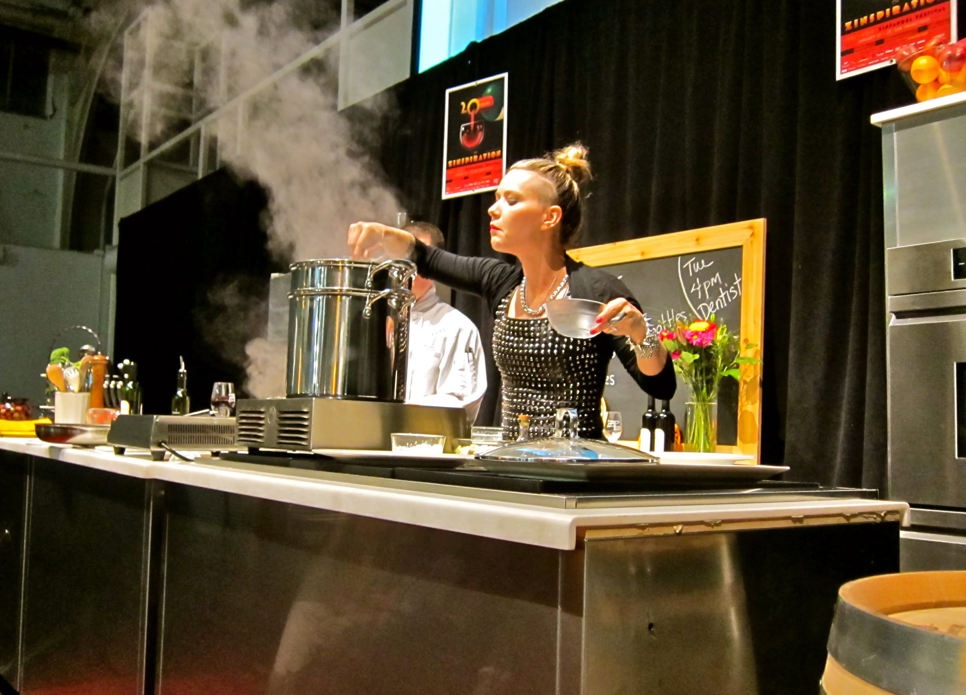 Woman cooking at a culinary event representing Lodi Winegrape Commission with steaming pot and kitchen setup.