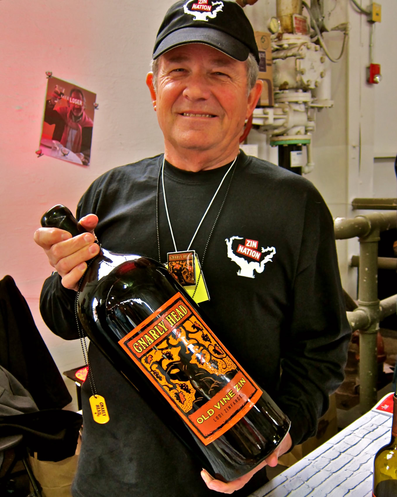 Man holding a large bottle of wine with Lodi Winegrape Commission label in winery setting.