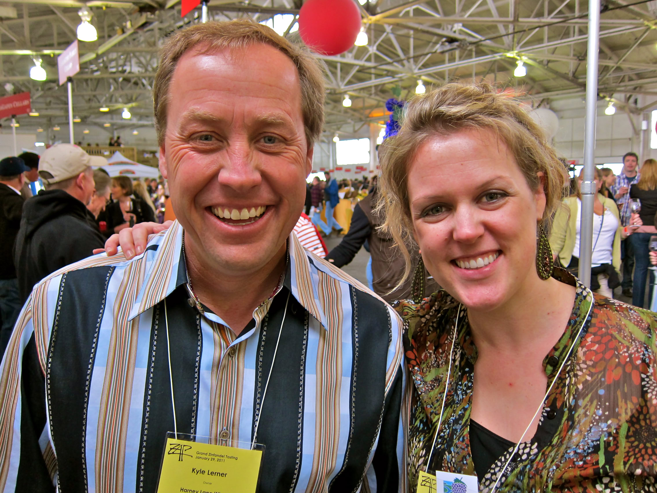 Two smiling individuals at a Lodi wine event, surrounded by a crowd and festive decorations.
