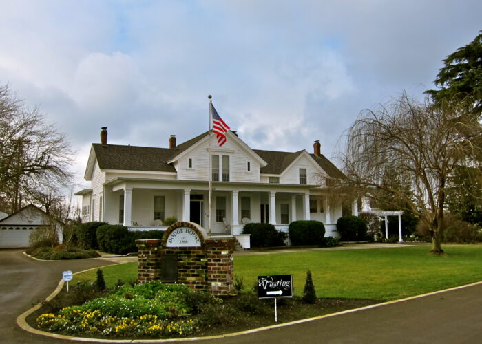 Historic white house with American flag, surrounded by trees and well-maintained lawn in Lodi, California.