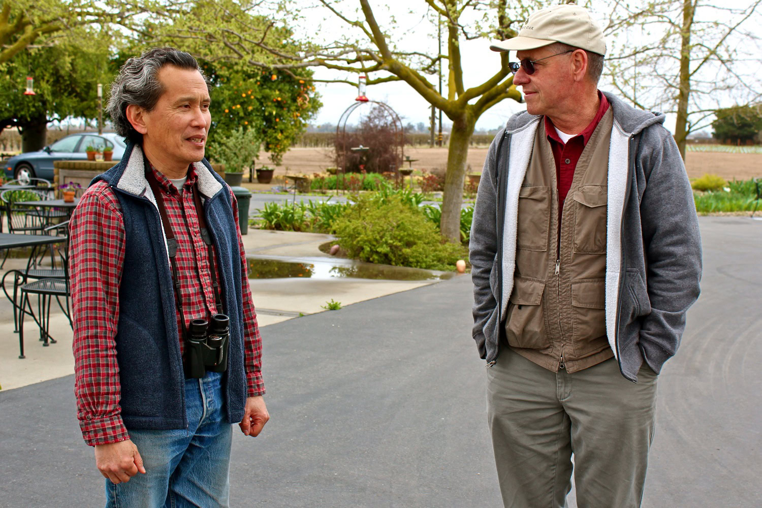 Two men conversing outdoors at a Lodi wine event, with vineyards in the background.