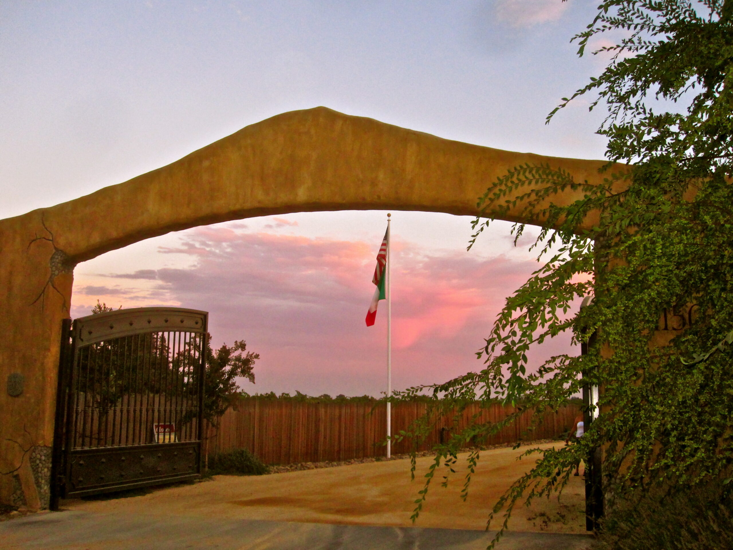 Entrance gate to Lodi Winegrape Commission with sunset sky and flag in the background.