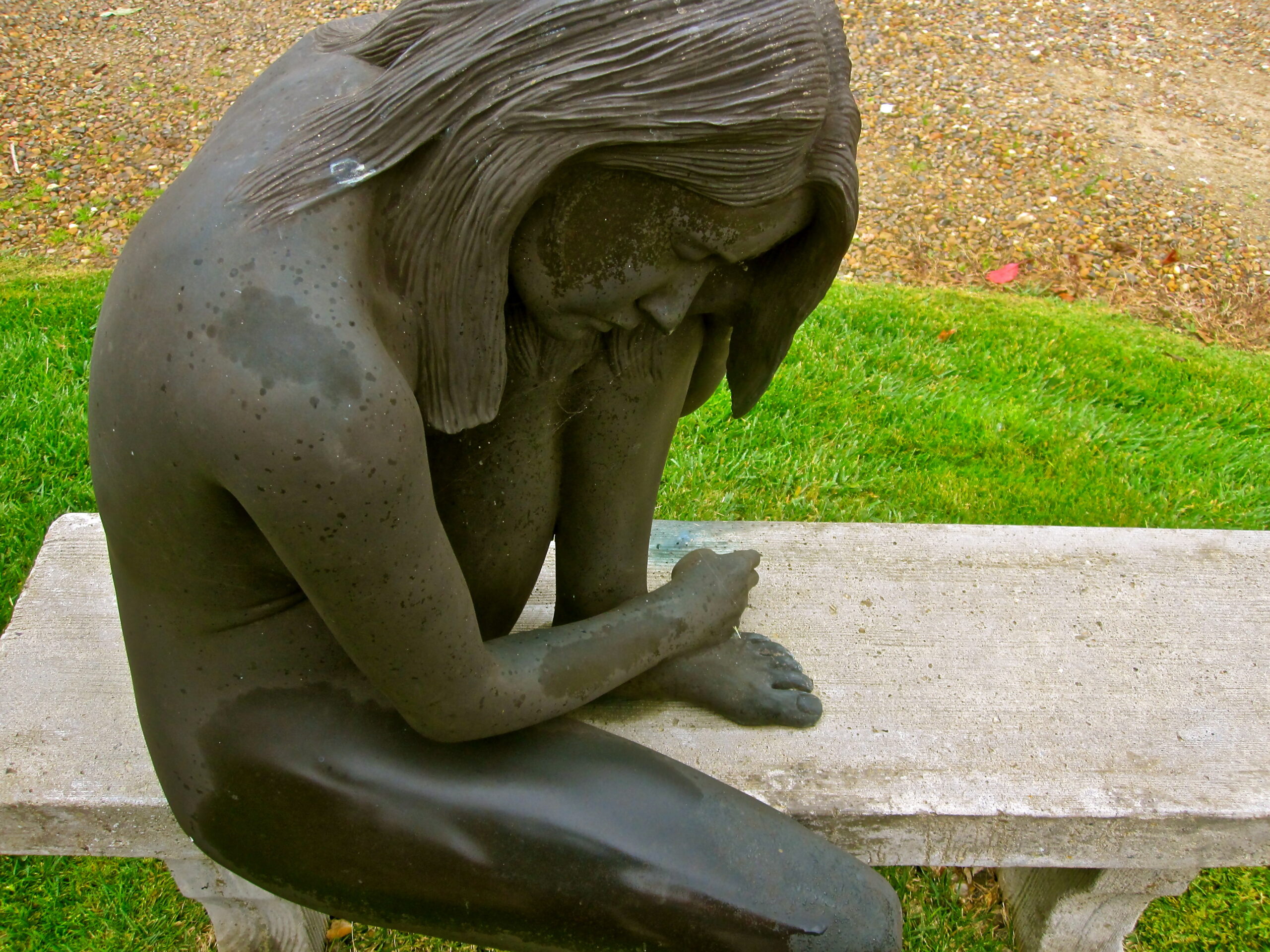 Bronze statue of a woman sitting on a bench, head bowed, in a reflective pose at Lodi Winegrape Commission.