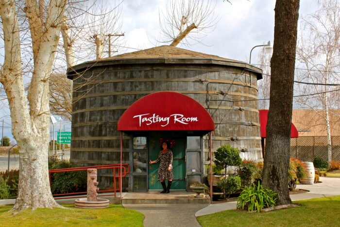 Woman entering the Lodi Wine Tasting Room with a red awning and rustic wooden exterior.