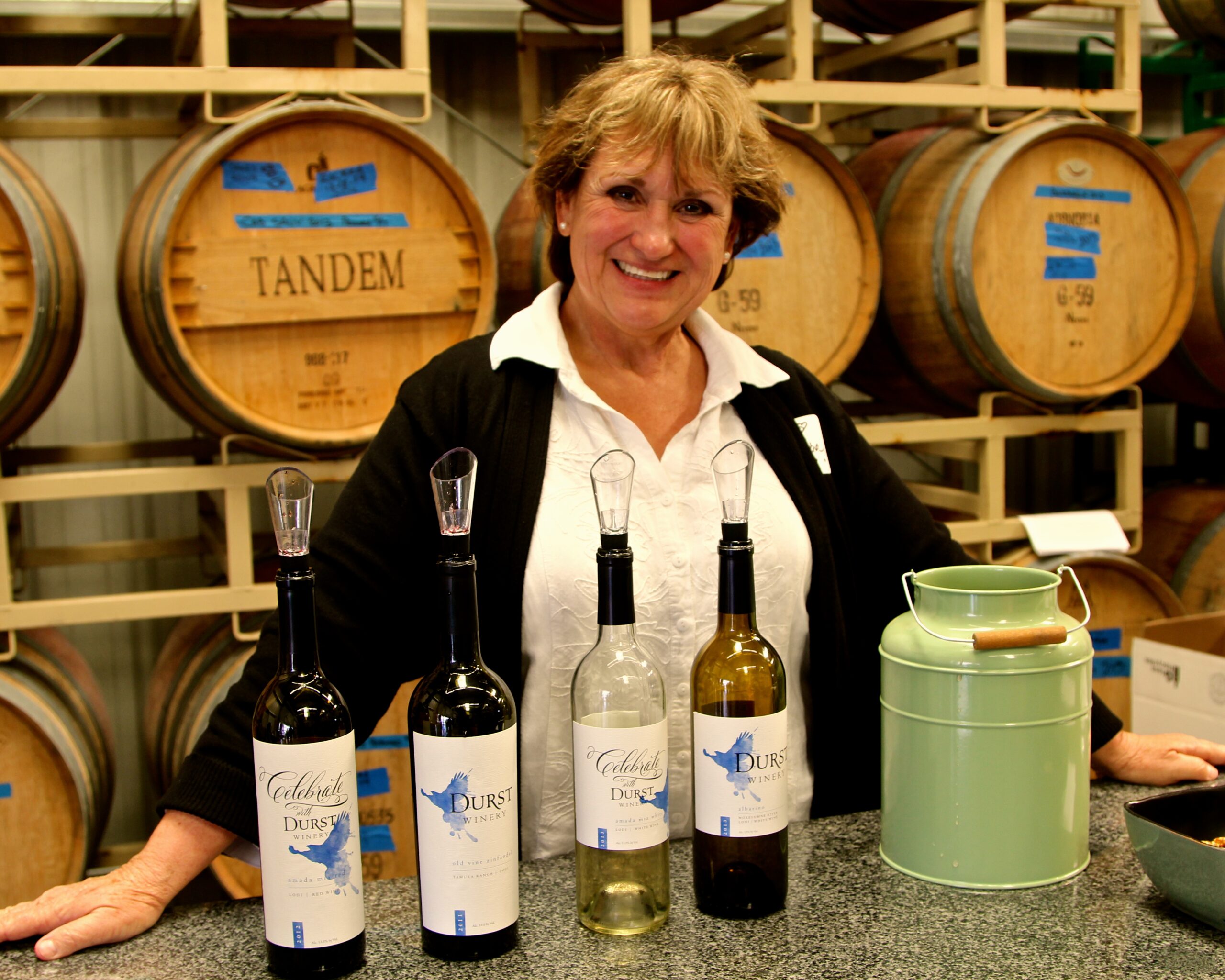 Woman showcasing Lodi wine bottles at a wine tasting event in a winery setting.