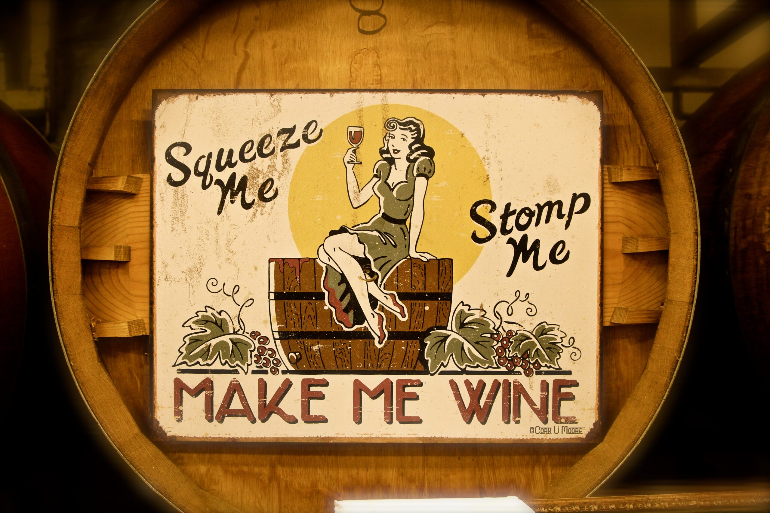Vintage-style sign promoting wine making with a woman holding a glass of wine, surrounded by wine barrels.