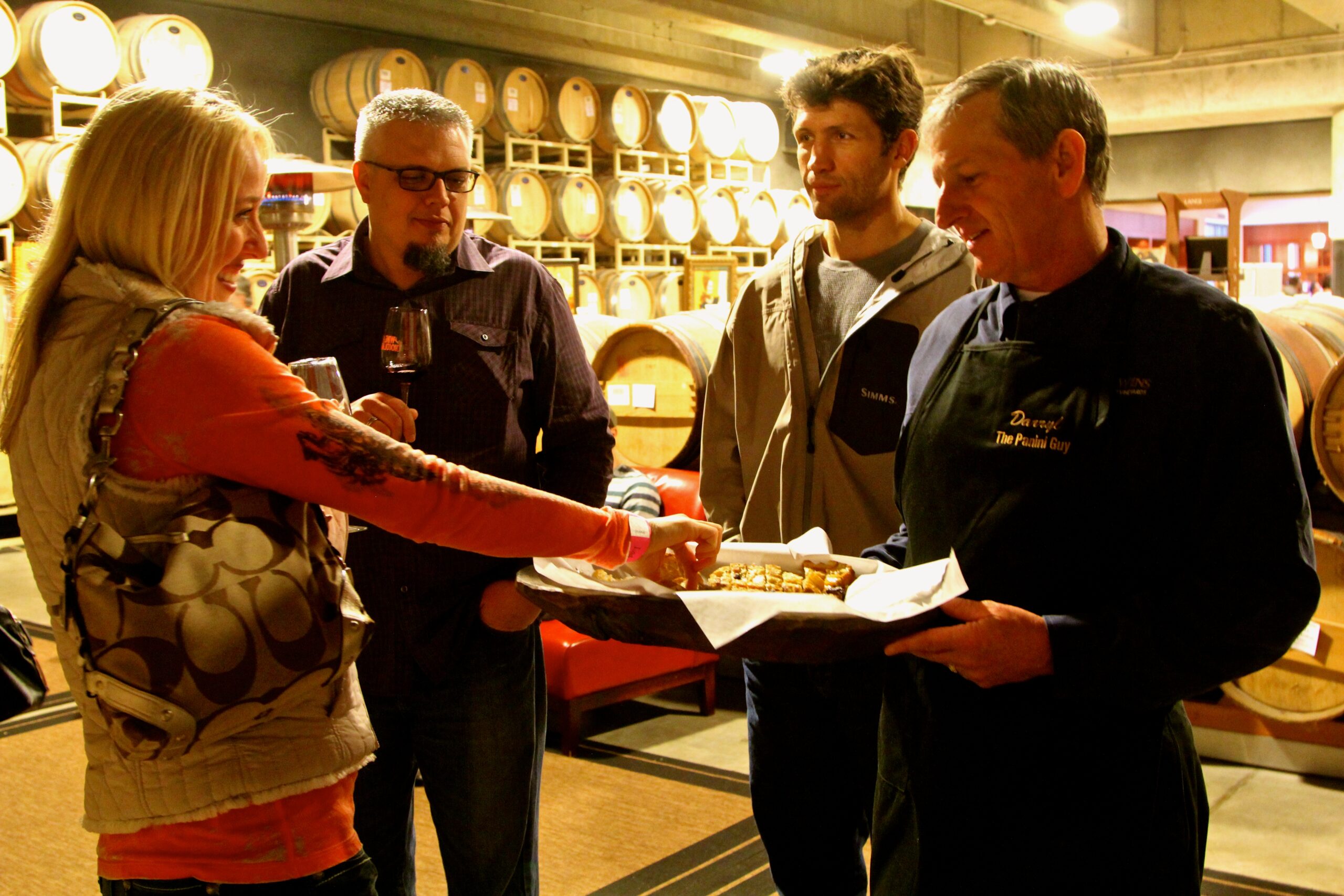 Group of people tasting wine at a winery with barrels in the background, representing Lodi Winegrape Commission activities.