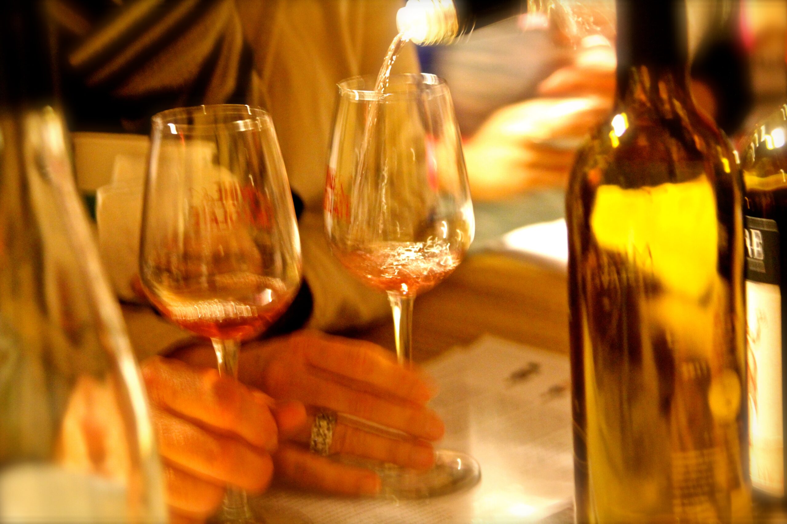 People tasting wine at a wine event, with glasses and bottles on the table.