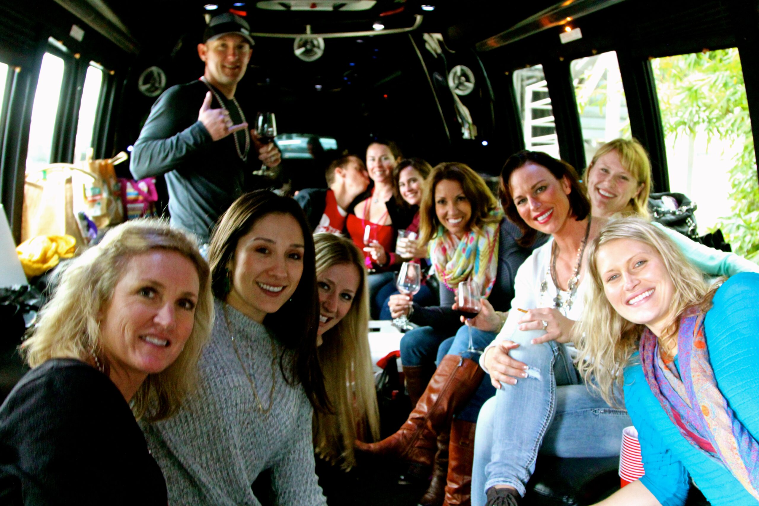 Group of people enjoying wine tasting tour inside a bus, smiling and holding glasses, in Lodi, California.