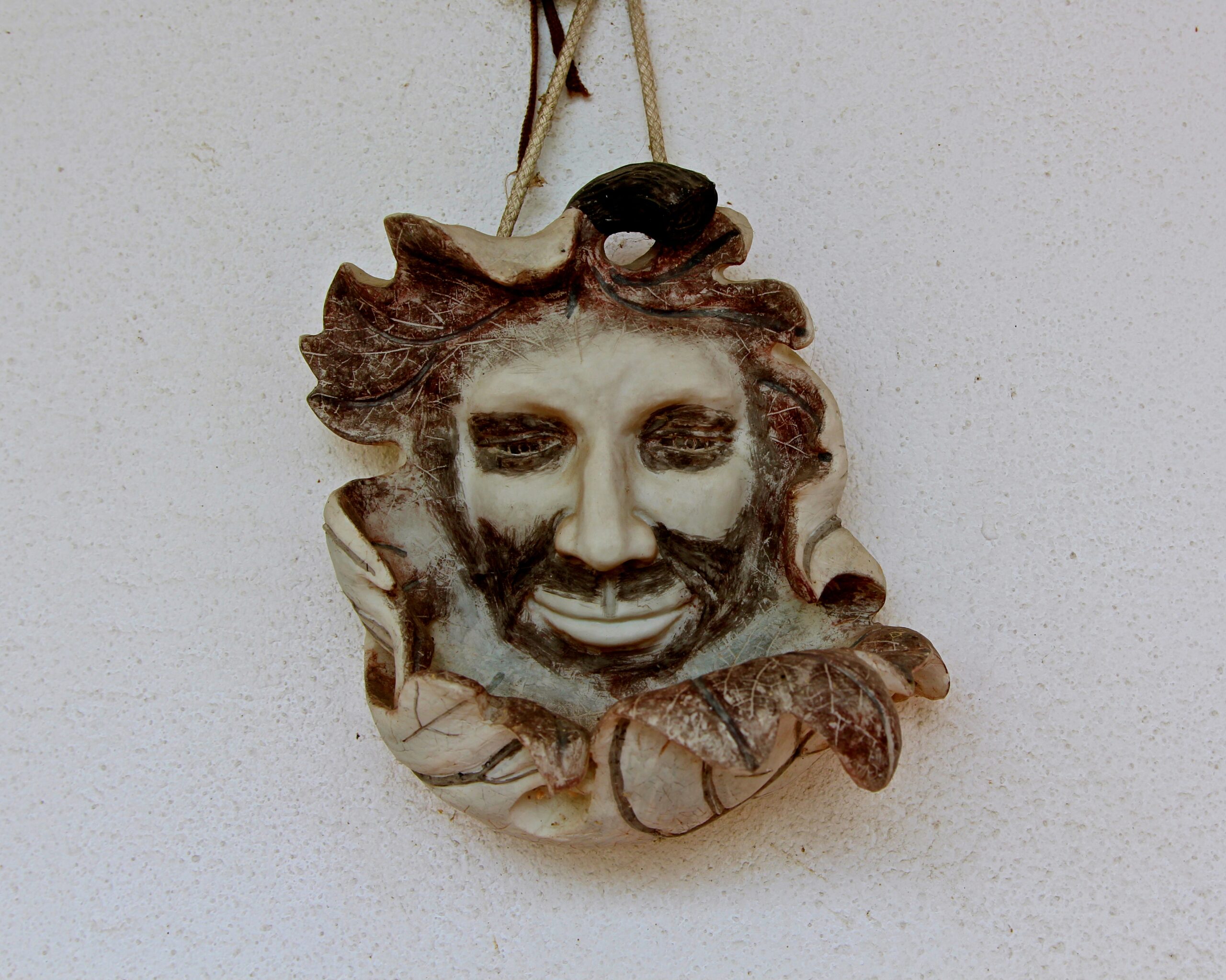 Decorative ceramic art featuring a human face with leaf details, hanging on a white wall.