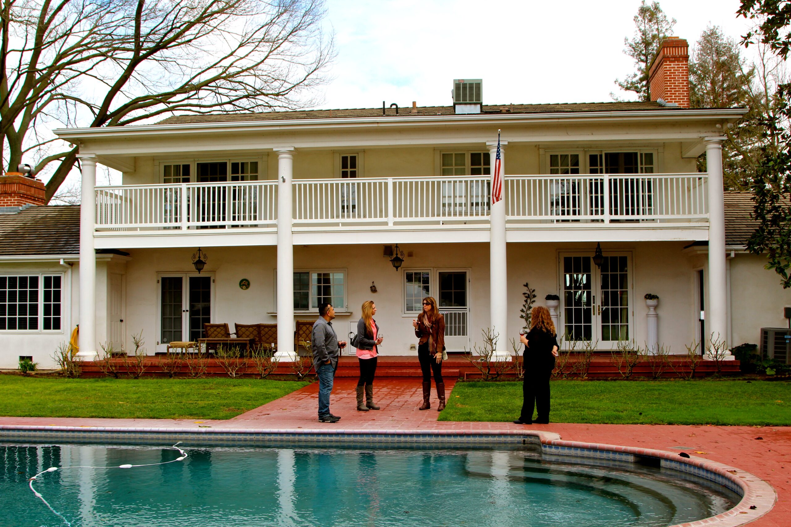Group of people talking outside the historic Lodi Winegrape Commission building with a swimming pool in the foreground.