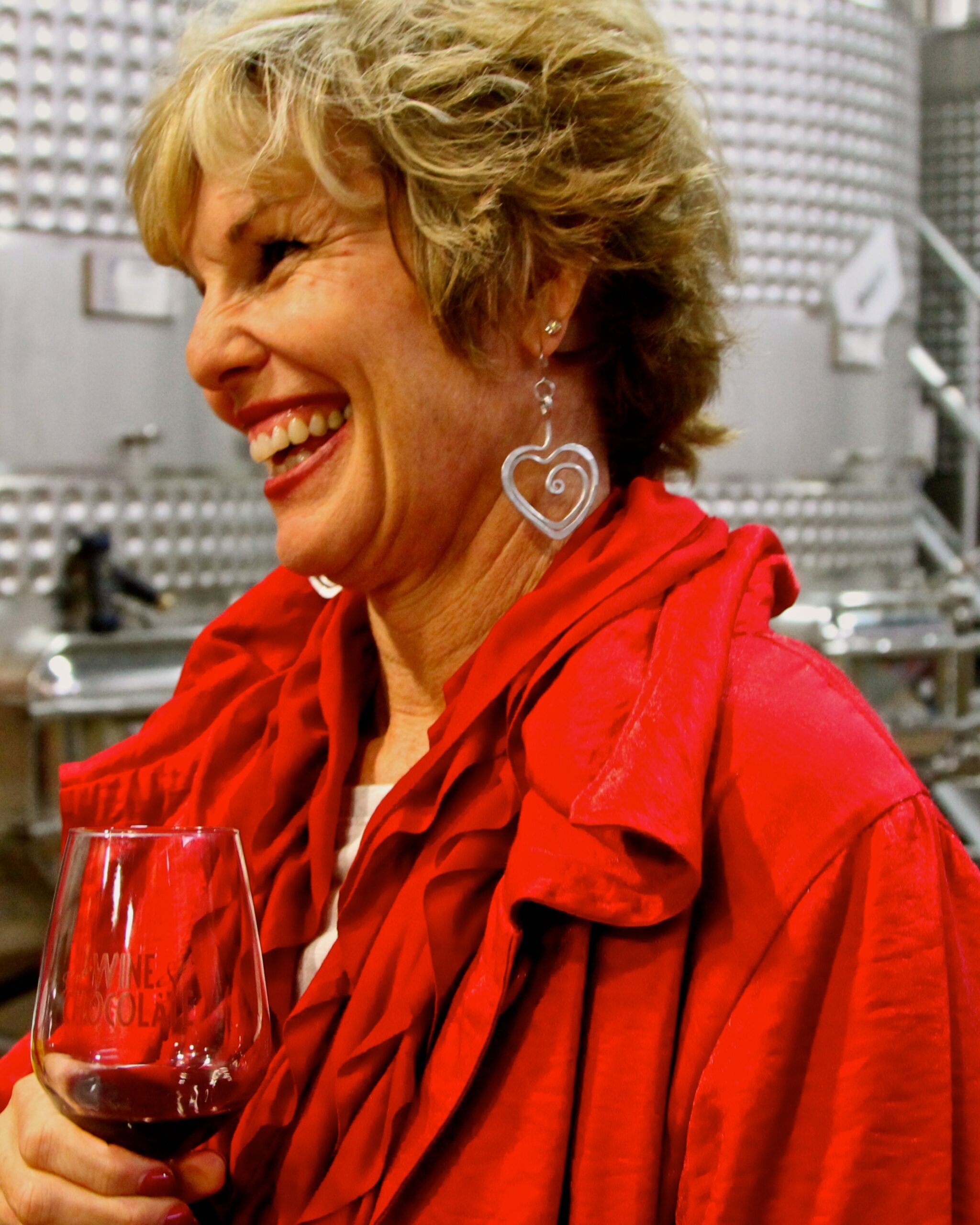 Smiling woman in red jacket holding a glass of red wine at a wine tasting event.