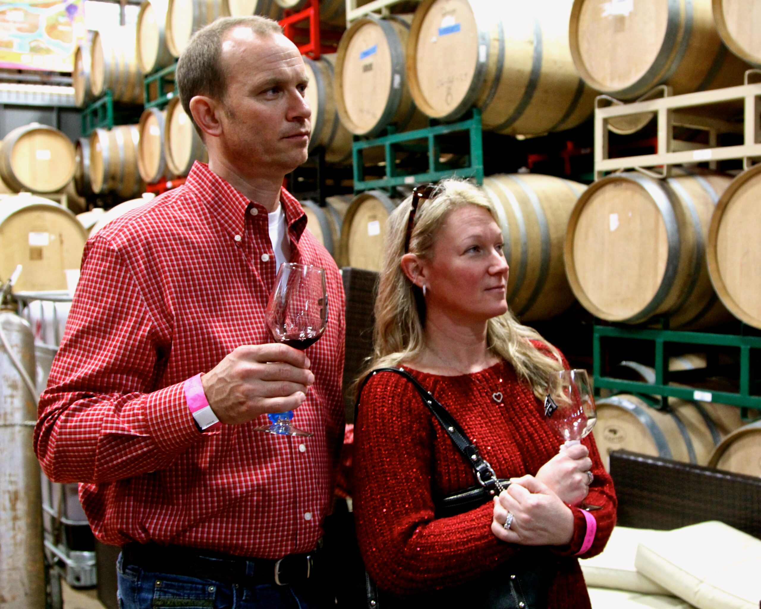 Man and woman tasting wine in a winery with wine barrels in the background.