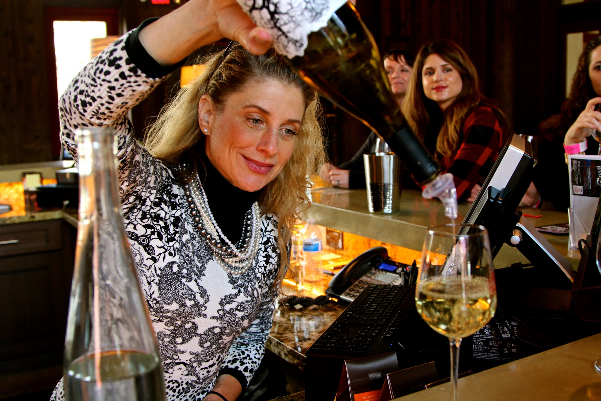 Woman pouring wine at Lodi Winegrape Commission event with guests in background.