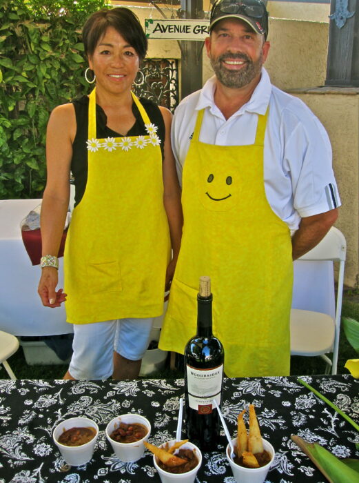 Two people wearing yellow aprons at a wine event with wine bottles and food on the table.