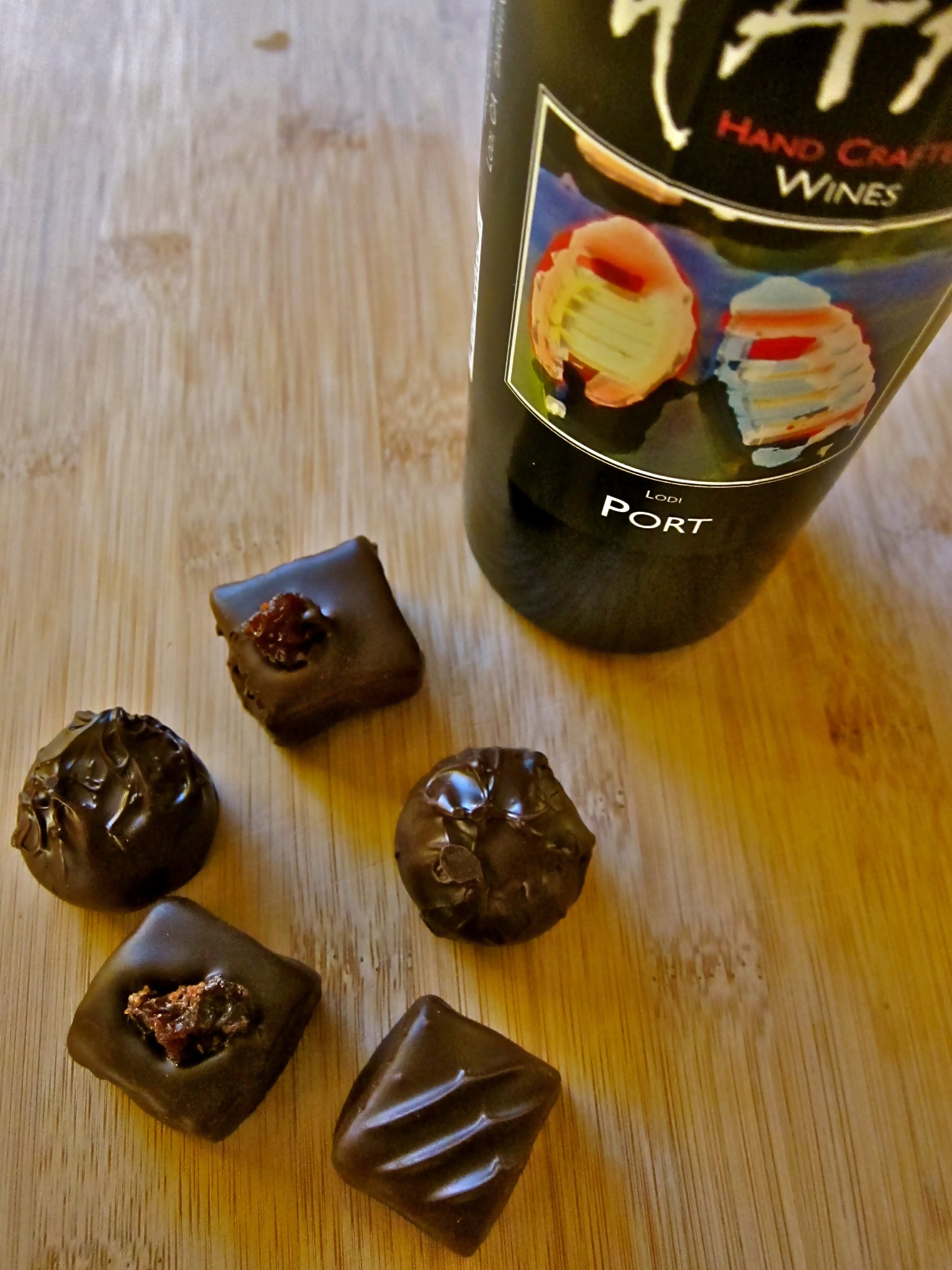 Bottle of Lodi Port wine with assorted chocolates on wooden surface.