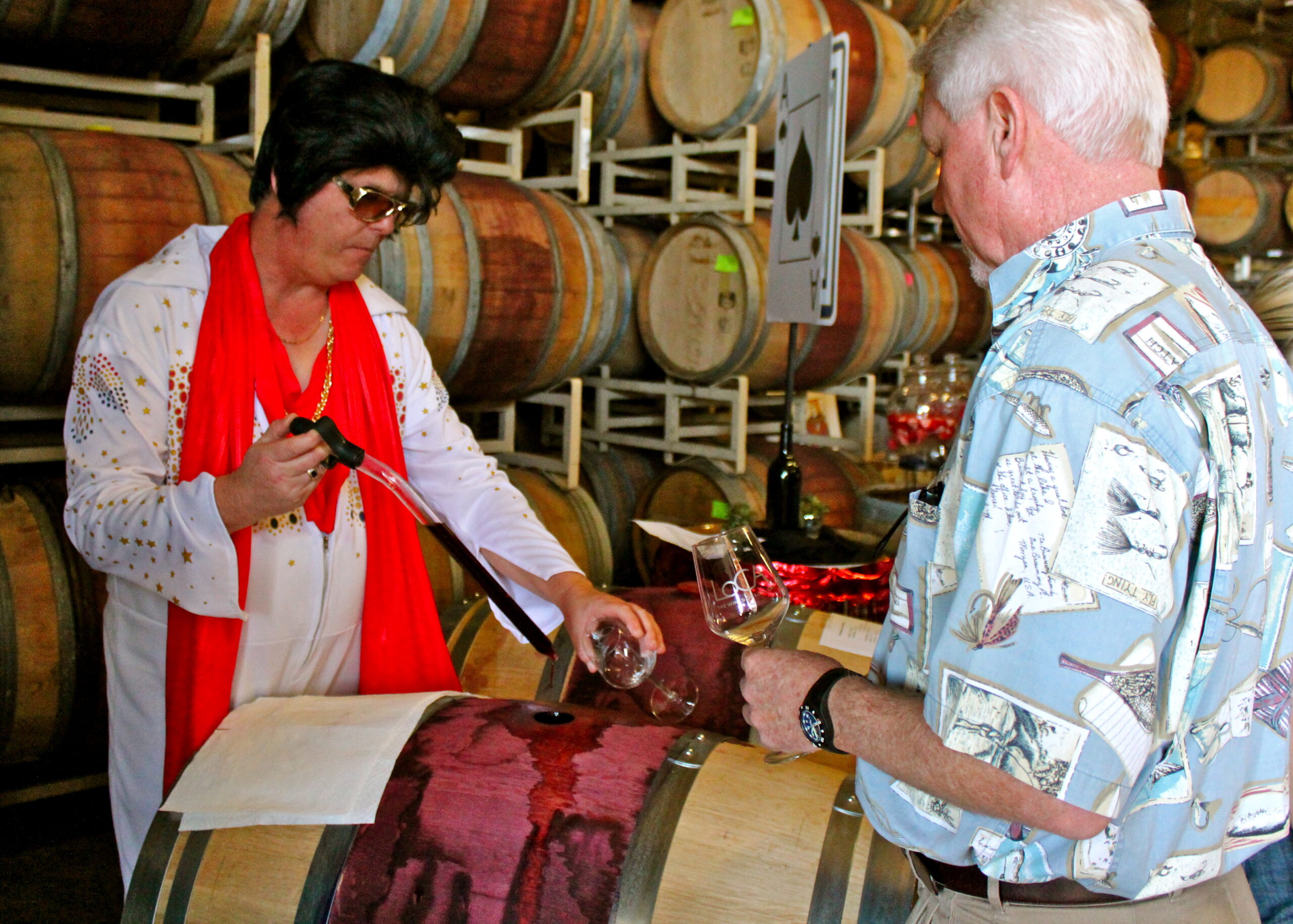 Wine tasting at a winery with barrels in the background, featuring a woman pouring wine for a man.
