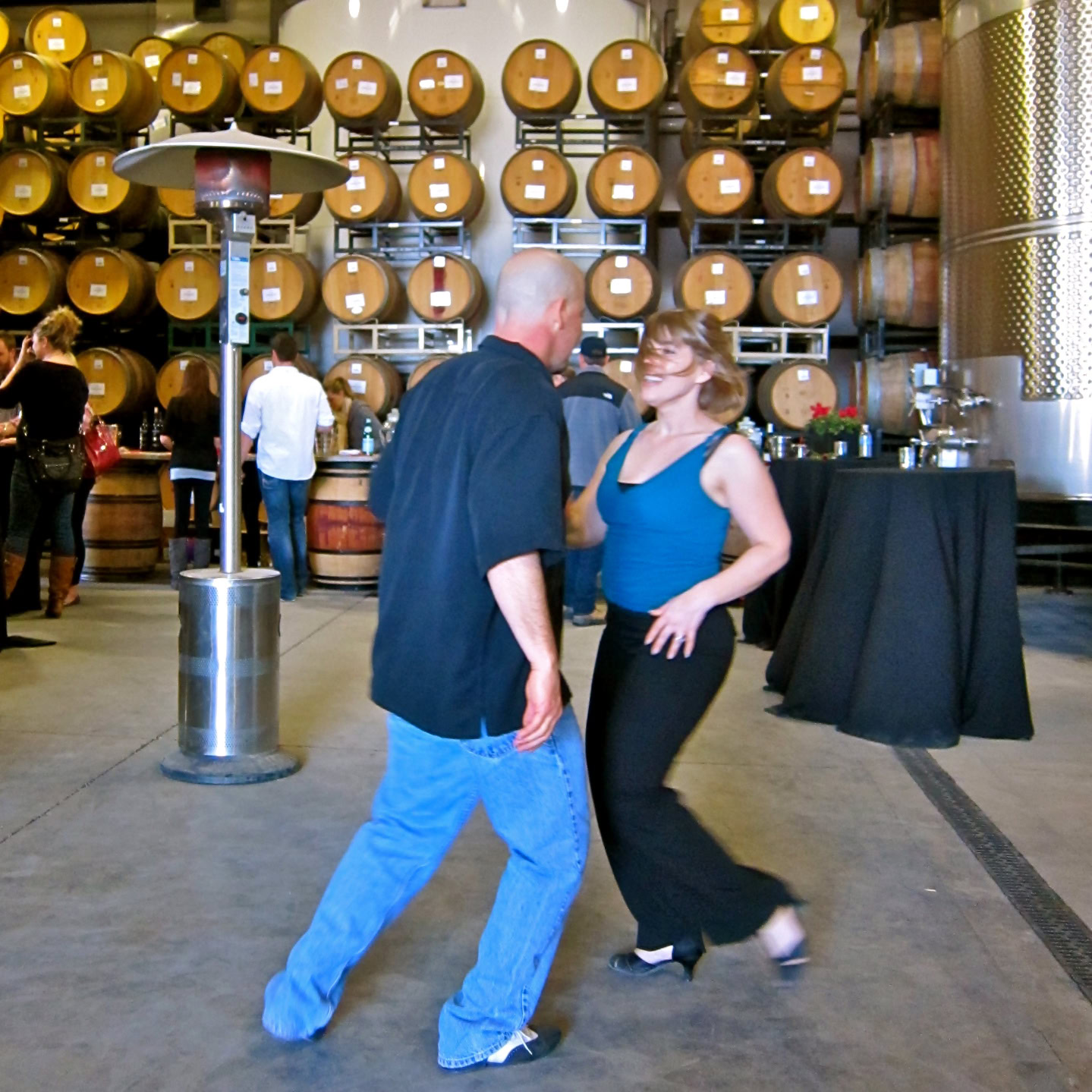 People dancing at a wine event with wine barrels in the background.