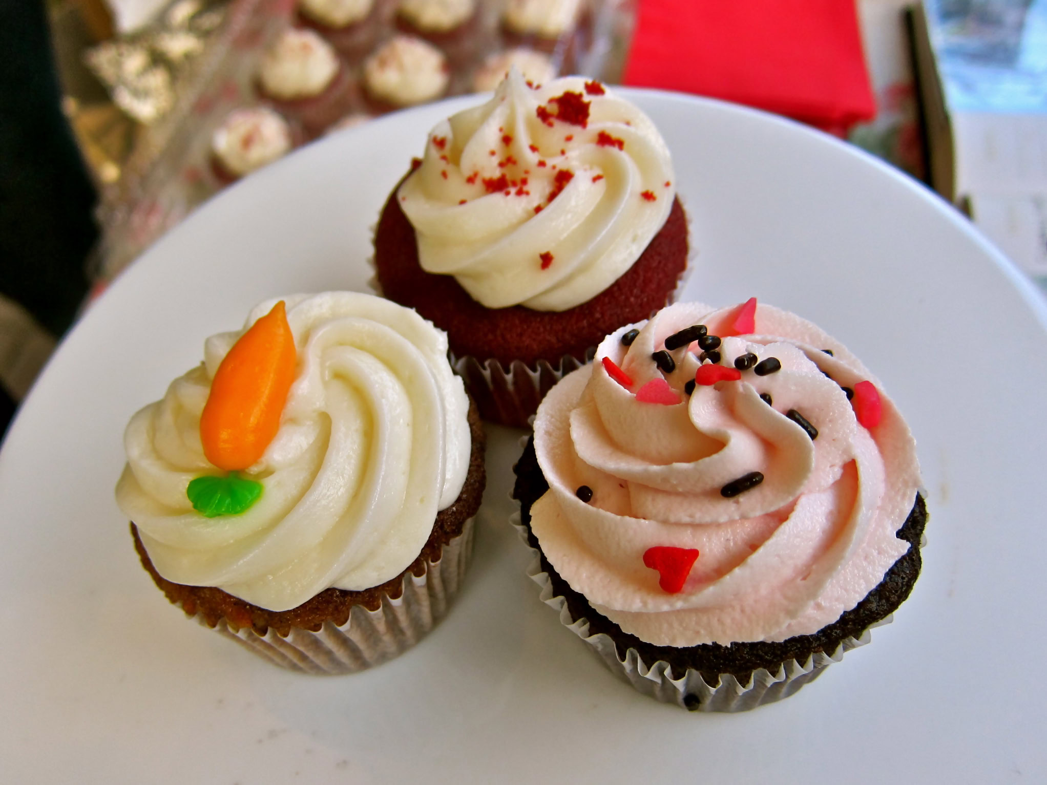 Three decorated cupcakes with colorful frosting and sprinkles on a white plate.