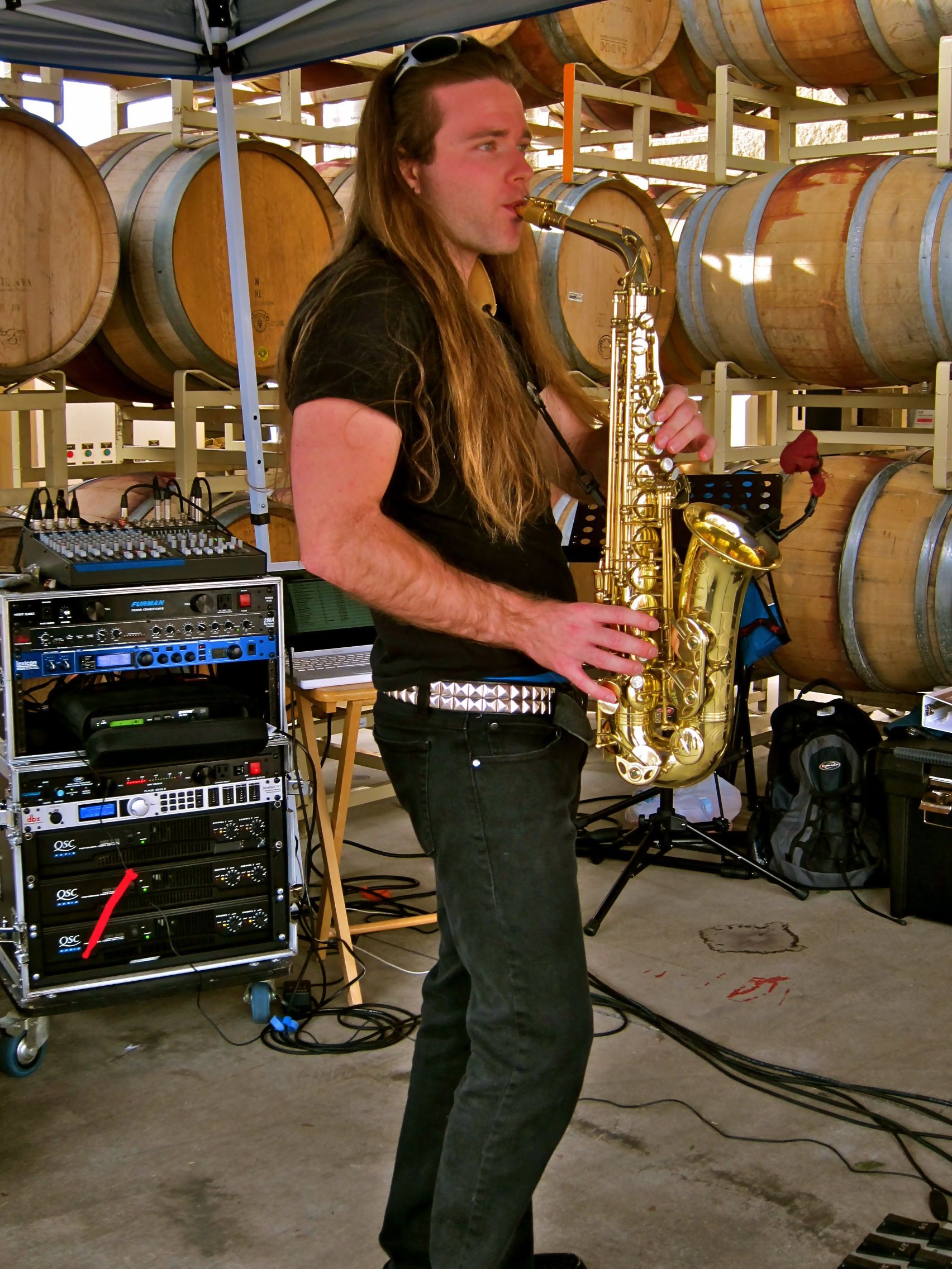 Musician playing saxophone at Lodi wine cellar with wine barrels in background.