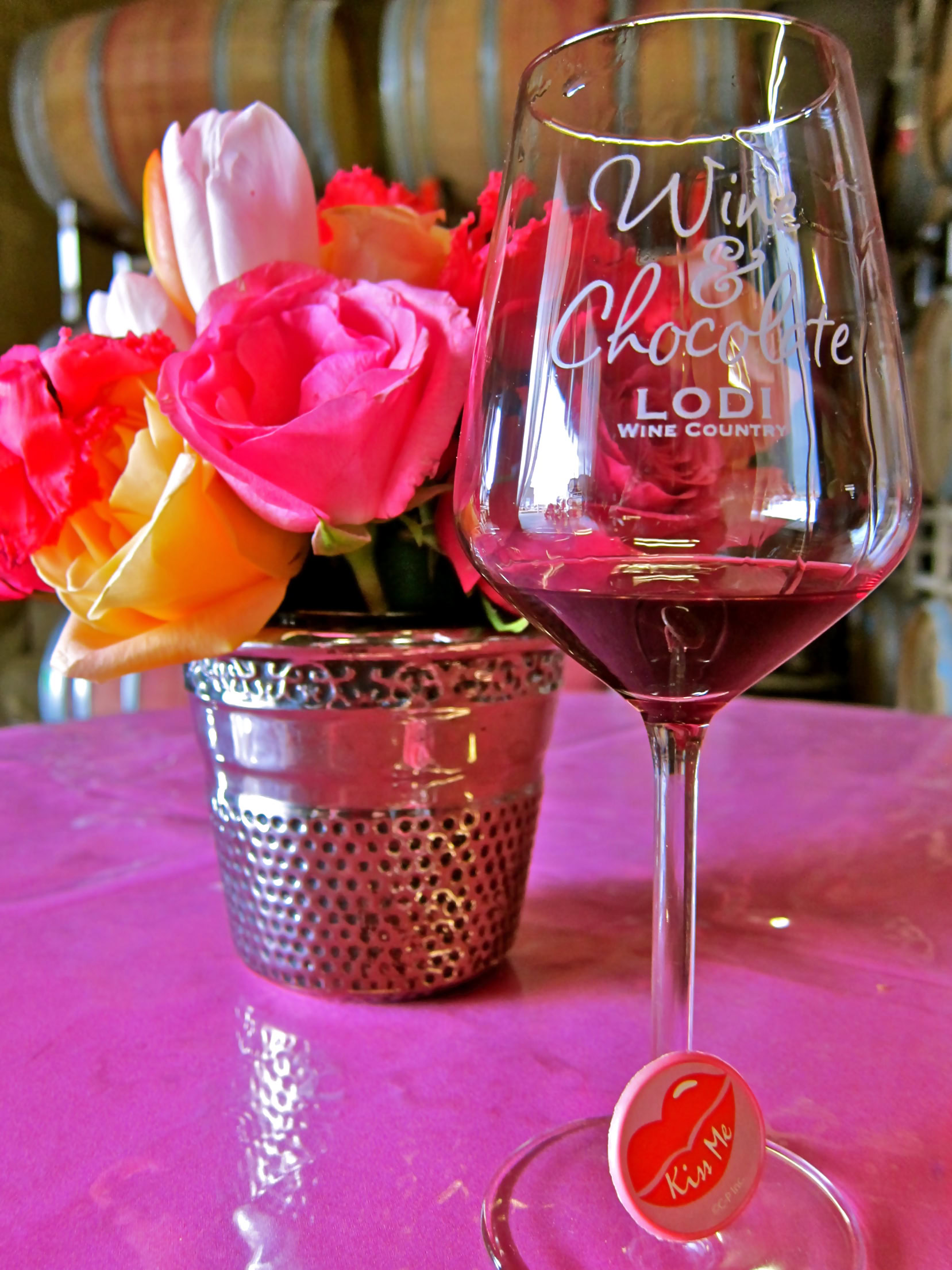 Glass of red wine with pink and yellow roses in background at Lodi Wine Country event.