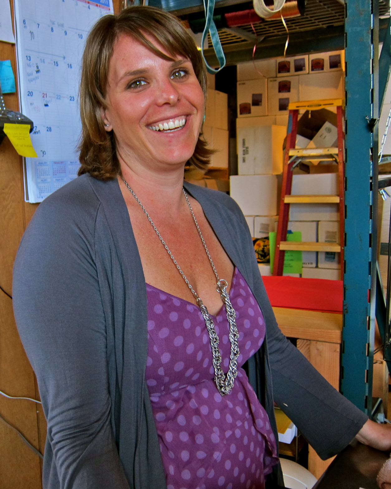 Smiling woman in a warehouse with wine storage shelves and boxes, representing Lodi Winegrape Commission.