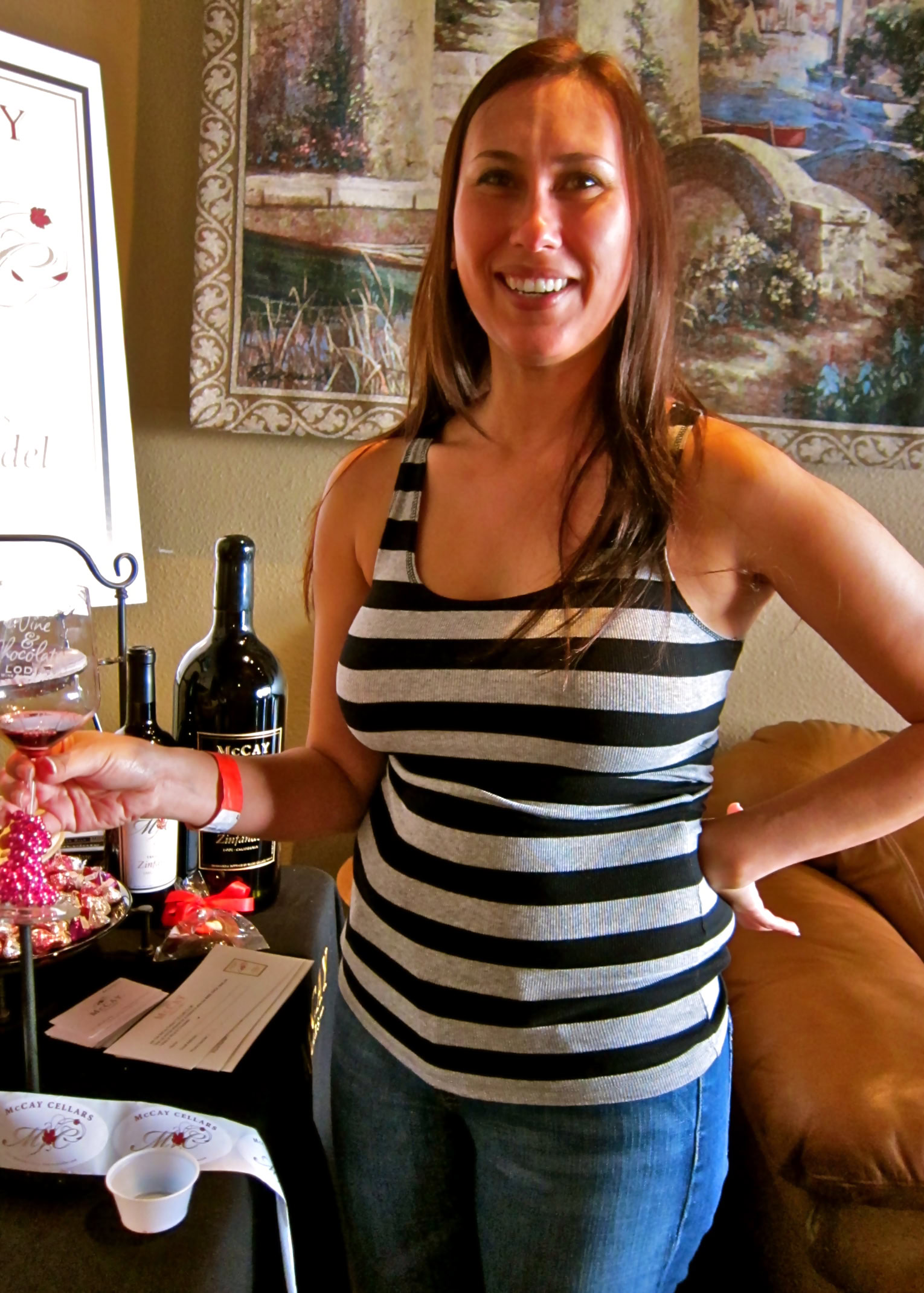 Smiling woman at Lodi Winegrape Commission event with wine bottles and snacks.