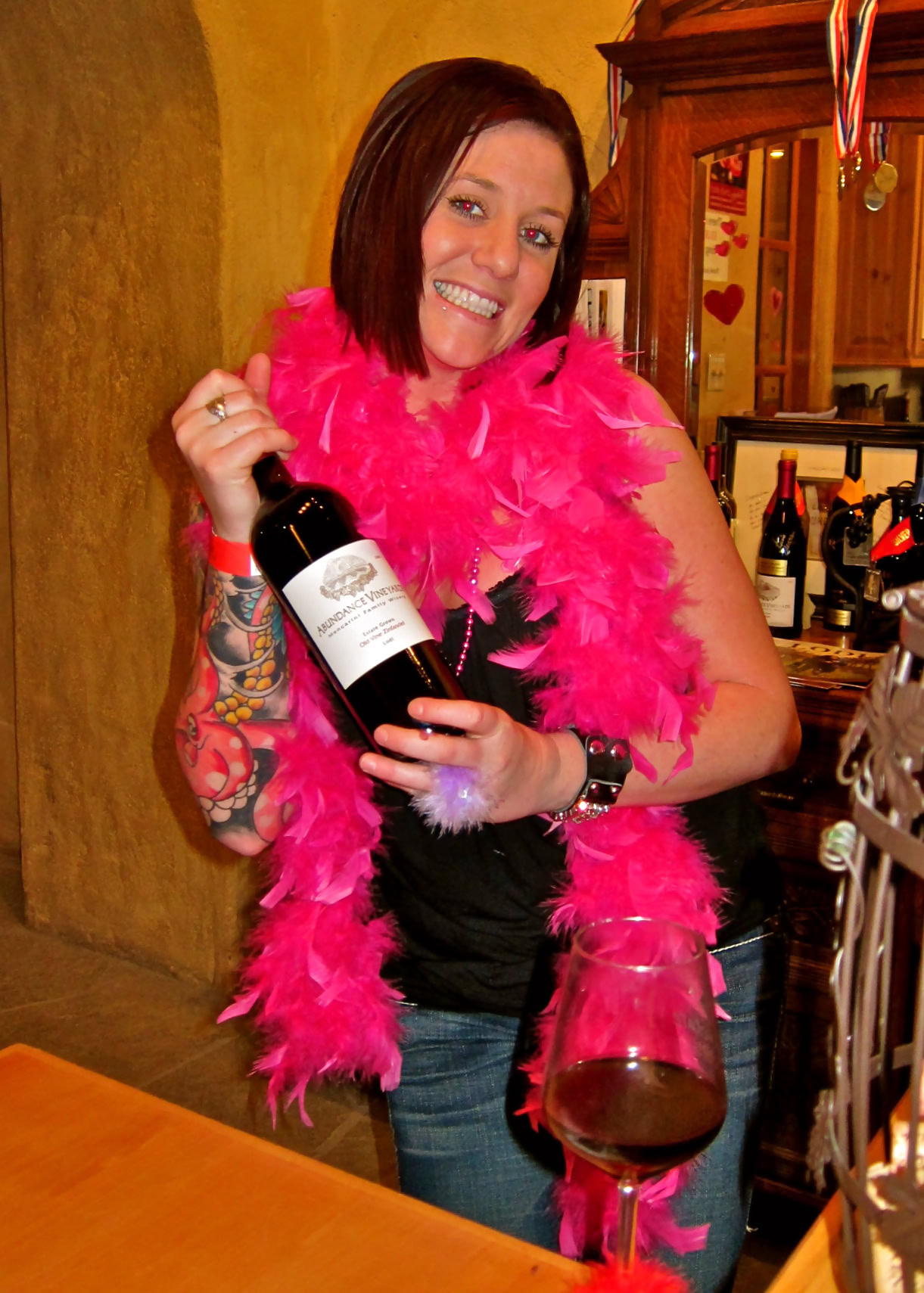 Woman with pink feather boa holding a wine bottle and glass at Lodi Wine event.