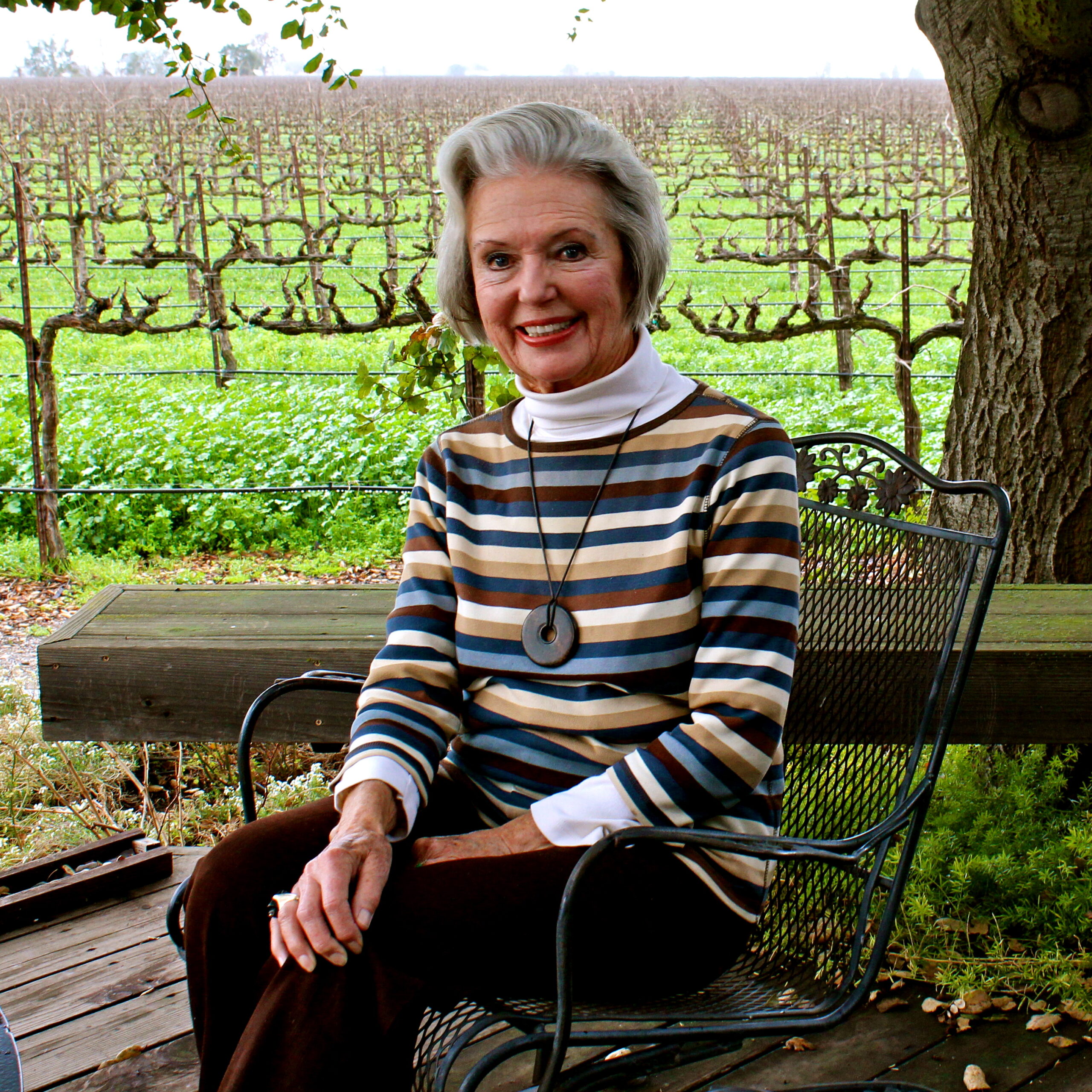 Woman sitting outdoors in vineyard with grapevines in the background, promoting Lodi wine and viticulture.