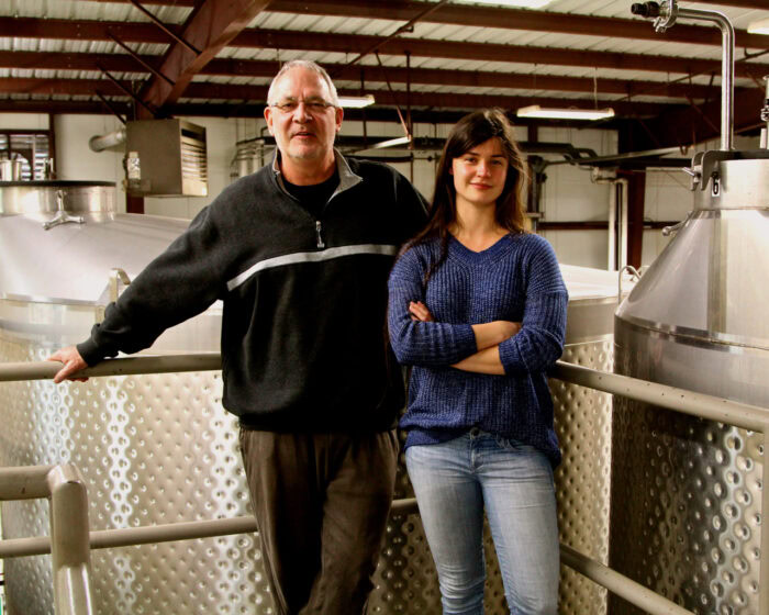 Two people standing inside a winery with large stainless steel fermentation tanks in Lodi, California.